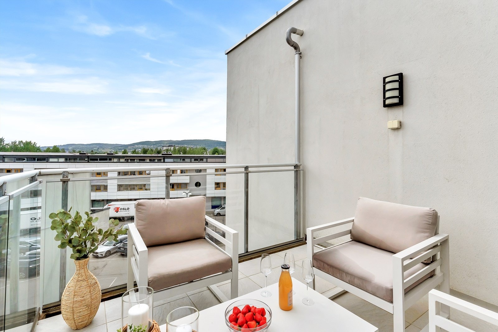 Romslig balkong med rekkverk i glass og fliser på gulv. Det er stikkontakt for utebelysning og varmeapparater. Galleribilde