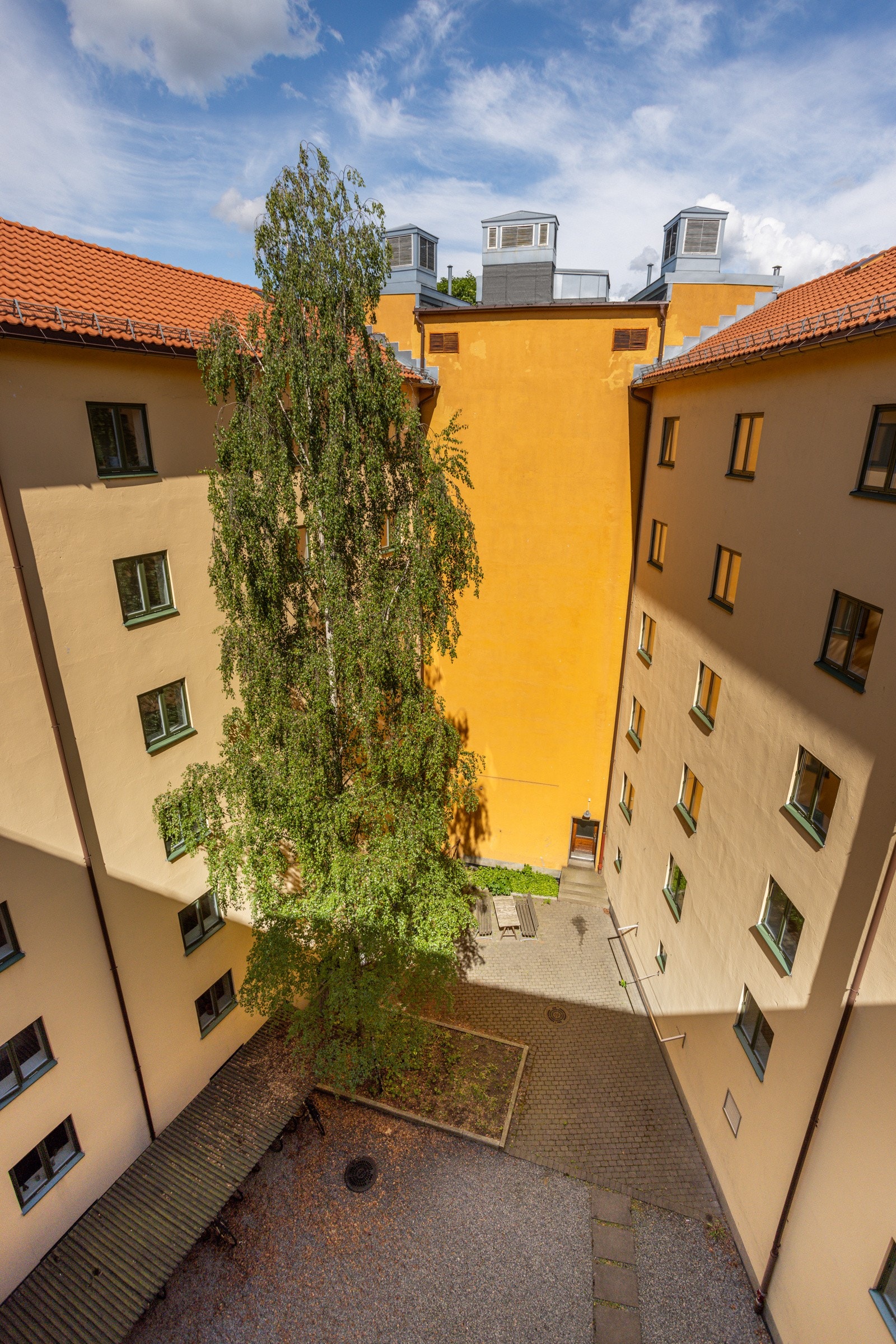 Felles tomt for borettslaget som består av bakgård opparbeidet med singel, belegningsstein, sykkelparkering, sittegrupper, busker og annen beplantning. Galleribilde
