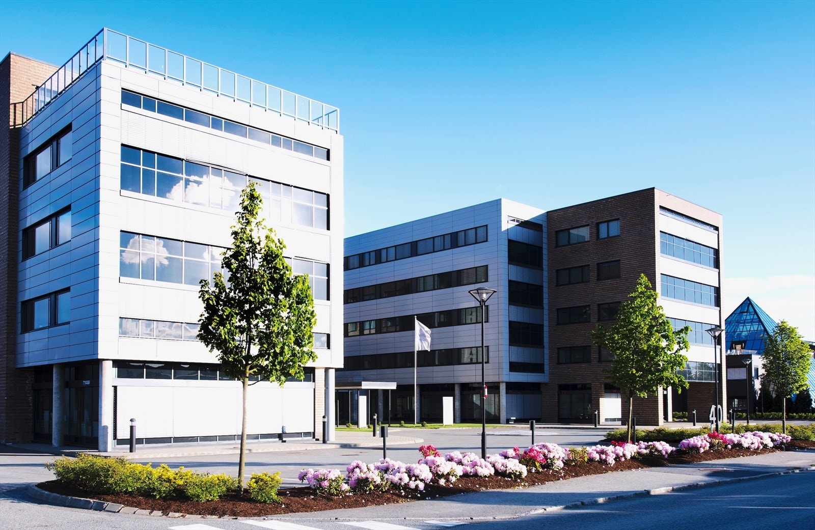 Moderne kontorbygg med attraktiv arkitektur, omgitt av velstelte grøntarealer og blomsterbed, i et dynamisk næringsområde. Galleribilde
