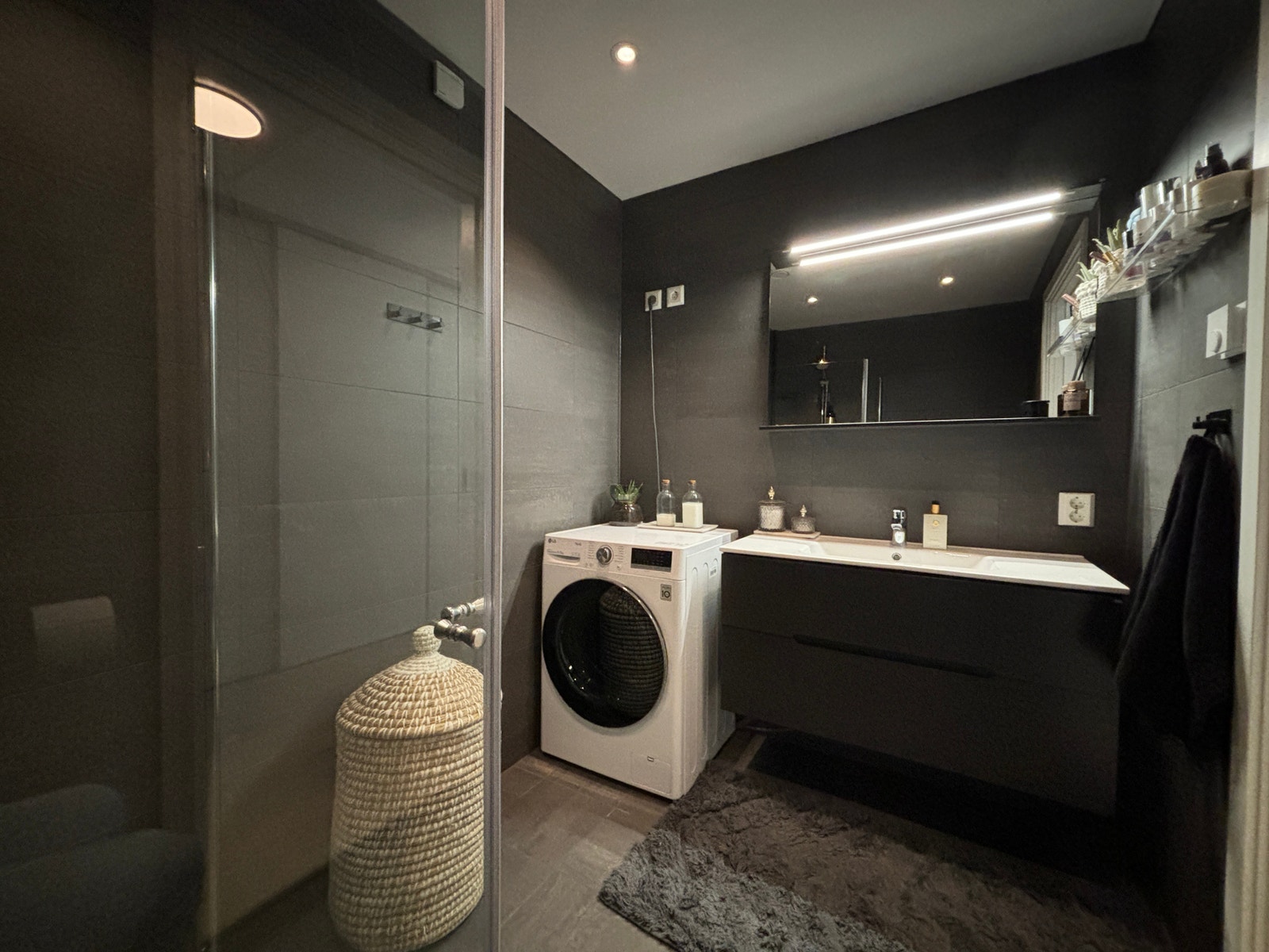 Badet er flislagt vegghengt toalett, dusjhjørne, servant og opplegg for vaskemaskin og tørketrommel. Galleribilde