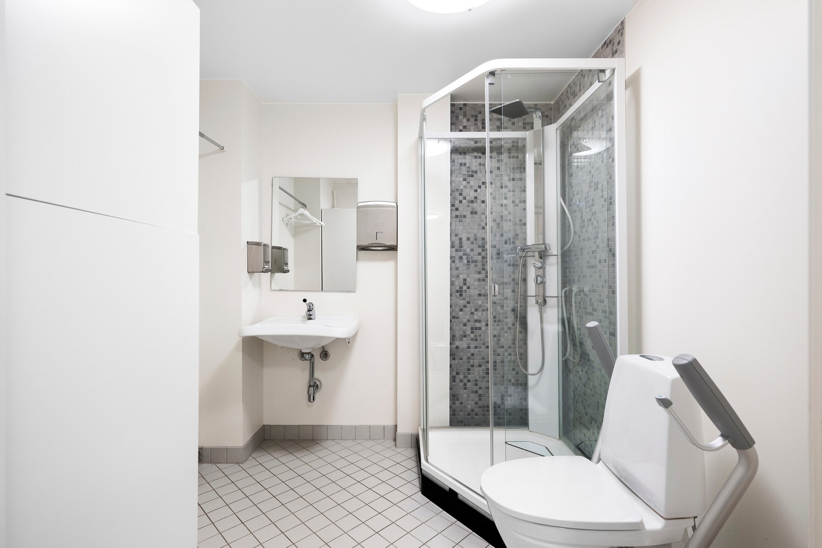 Større, delvis flislagt baderom med wc, dusj og baderomsskap. Galleribilde