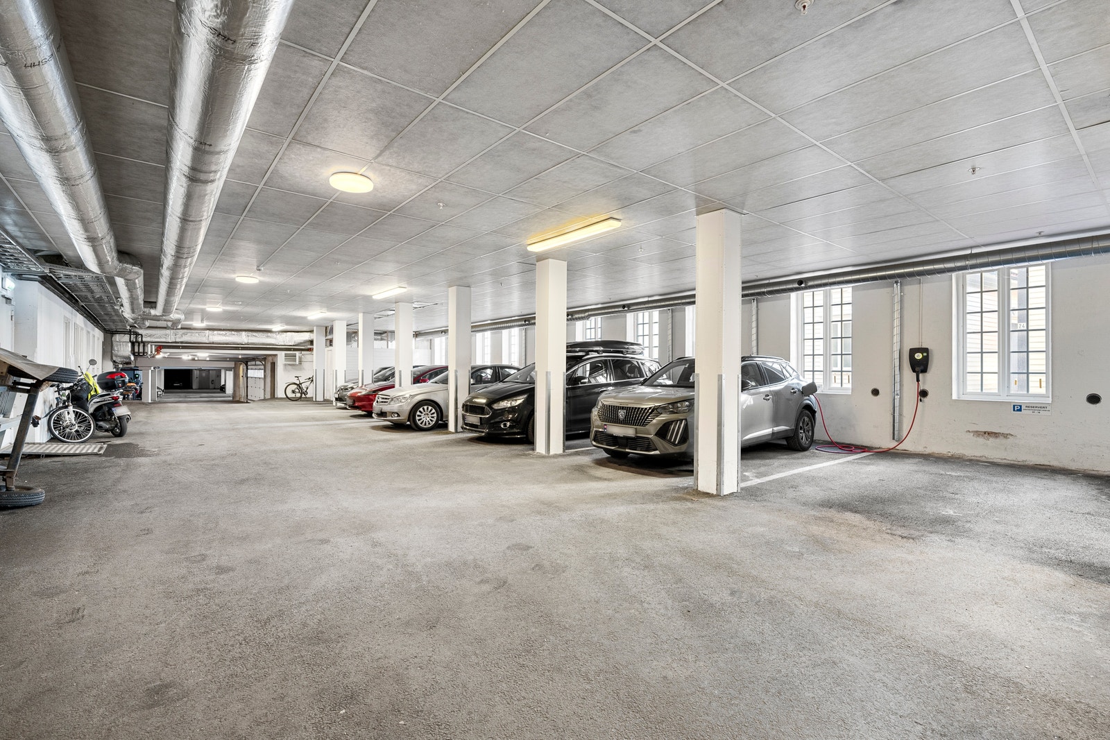 Oppvarmet garasjeanlegg med 4 faste plasser tilhørende seksjonen. Automatisk portåpner medfølger. Arkivrom, felles avfalls- og teknisk rom samt sykkelparkering i tilknytning til garasjeanlegg. Mulighet for installasjon av elbil-ladere. Galleribilde