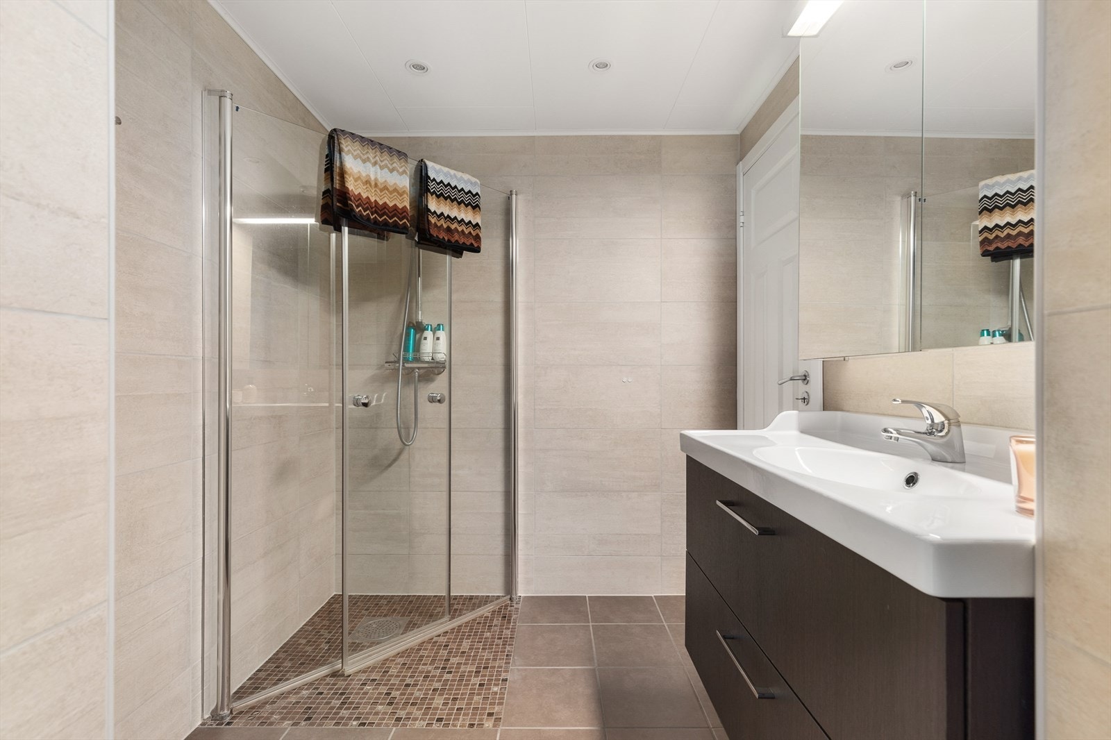 Det stilrene baderommet er på 5 m² og er innredet fra topp til tå med et delikat flisvalg på vegger. Her har man gulvvarme som skaper en lun og behagelig plass å være. Det er etablert moderne downlights i tak for en optimal lyssetting. Galleribilde