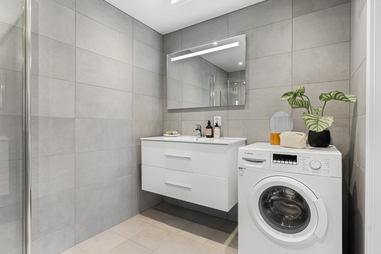 Videre består innredningen av et dusjhjørne med innfellbare dører i glass, og vegghengt klosett. Det er også opplegg for vaskemaskin på badet. Galleribilde