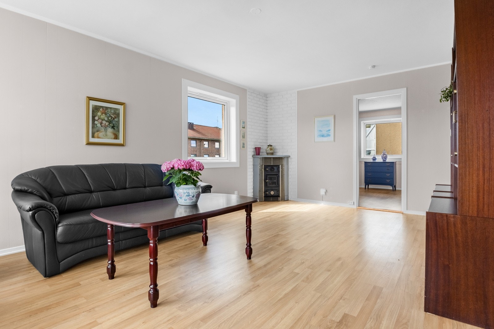 I hjørnet av rommet er det plassert en vedkamin mot brannmur kledd i hvitmalt teglstein. Pipene ble rehabilitert i regi av brl. i 2021. Galleribilde