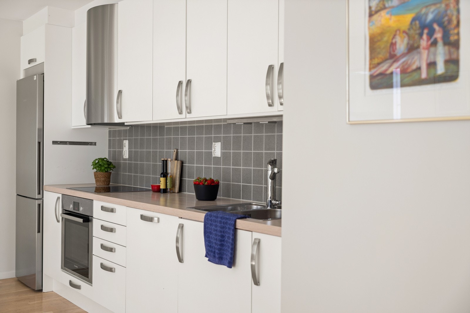 Kjøkkenet består av innredning med slette fronter, benkeplate av laminat, nedfelt oppvaskkum med ett-greps kran, fliser mellom kjøkkenbenk og overskap, samt benkeskapsbelysning og stikkontakter under overskap. Galleribilde