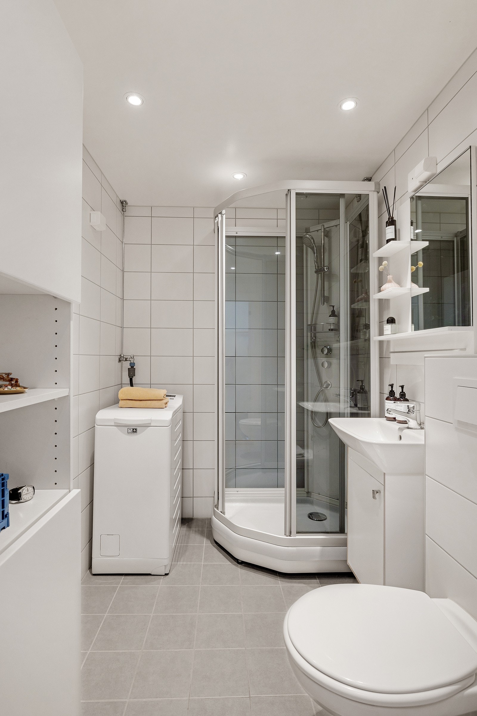 Baderommet har lys grå fliser på gulv med gulvvarme, lyse fliser på veggene og downlights i himlingen. Galleribilde