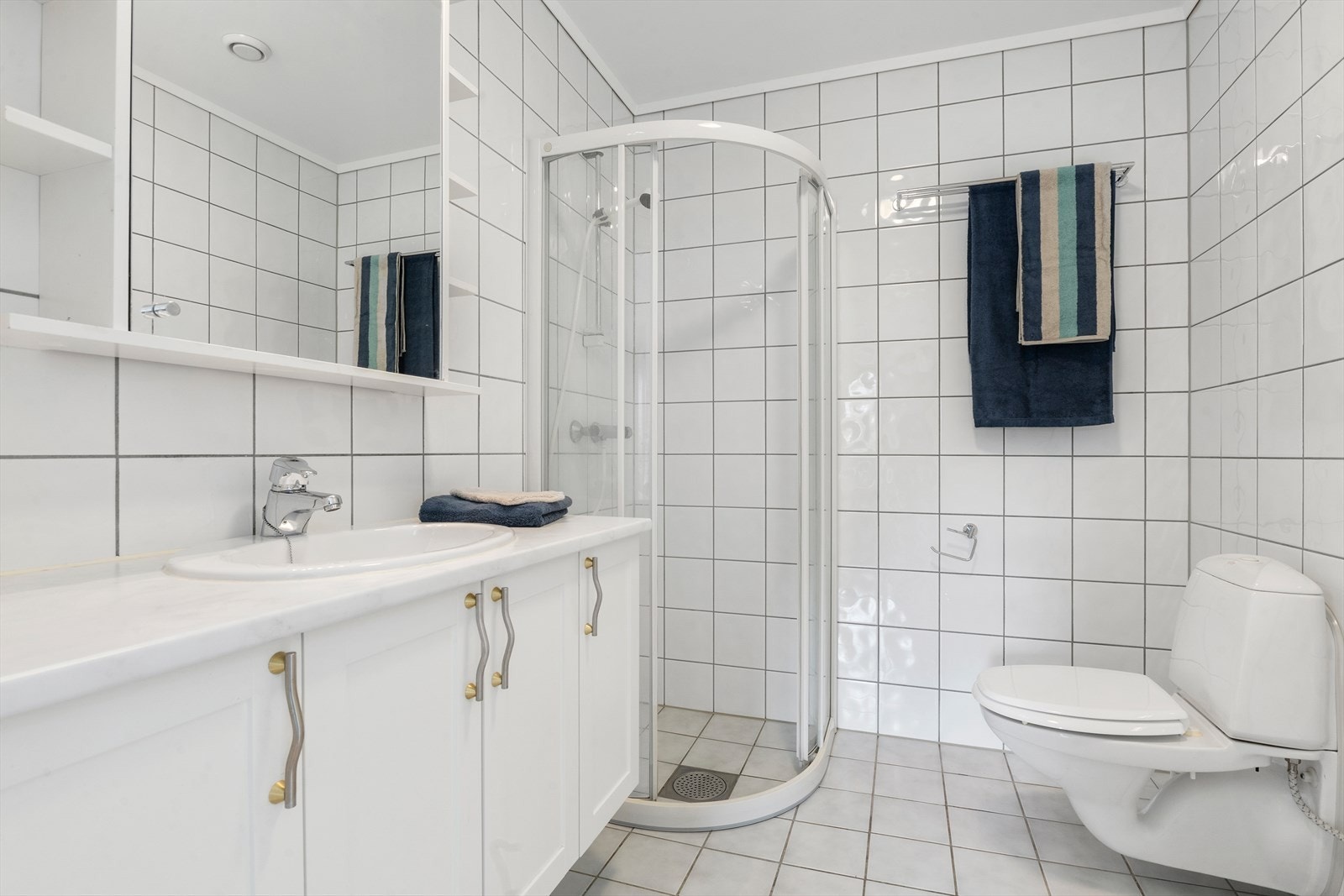 Bad/vaskerom er innredet med vegghengt toalett, dusjhjørne og innredning med servant. Galleribilde