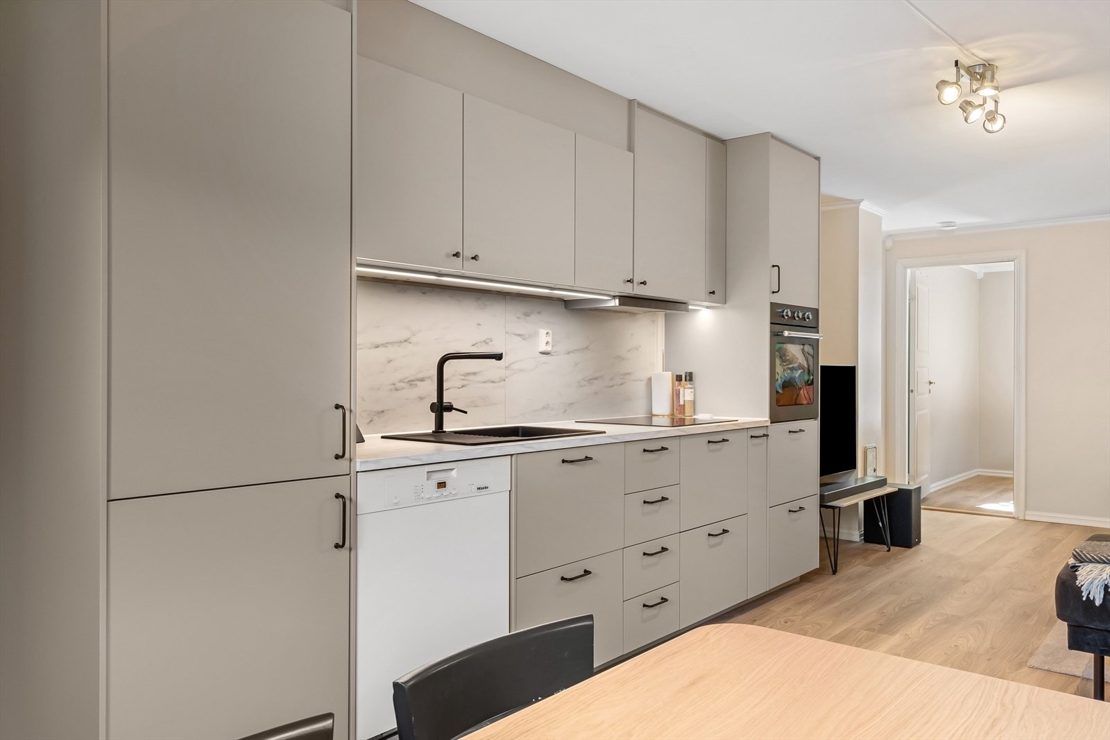 Ny kjøkkeninnredning med glatte fronter og hvitevarer i 2024 samt benkeplate av laminat med nedfelt vaskekum og induksjonstopp - Det er integrerte hvitevarer med kjøl/fryseskap, stekeovn og Mièle oppvaskmaskin Galleribilde