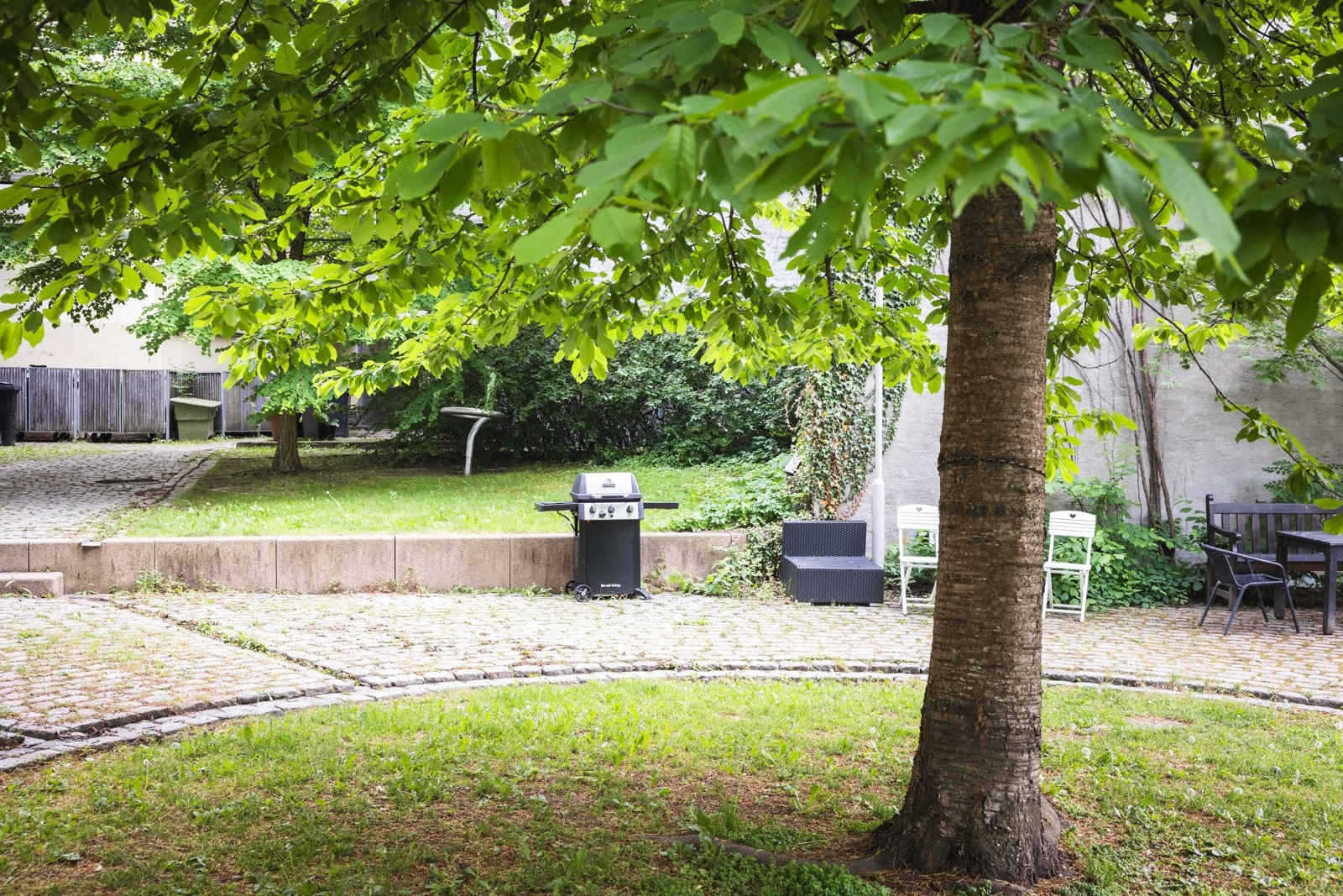 Pent opparbeidet bakgård med gressplen, trær, beplantning, grill og sittegrupper. Galleribilde
