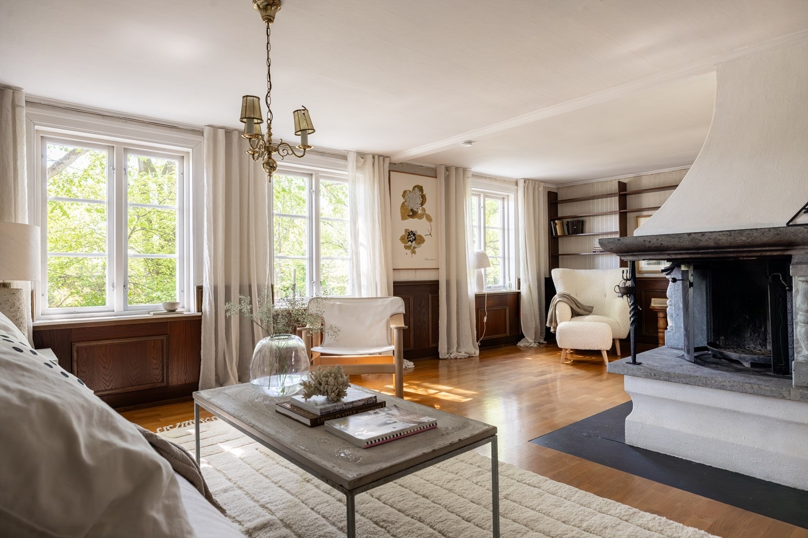 Andre etasje har en svært stor stue som er ideell for avslapning og sosiale sammenkomster. Peisen som har vakre detaljer i kleberstein er et naturlig midtpunkt som gir rommet god varme, og det er god plass til flere sosiale soner. Galleribilde