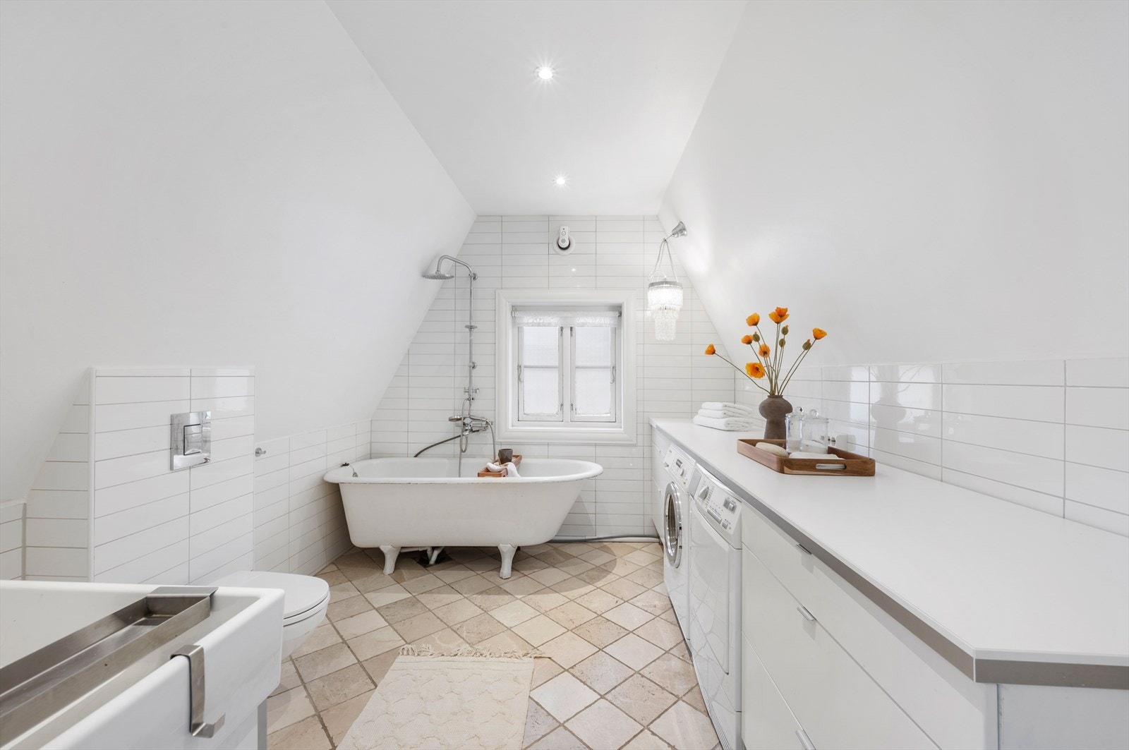 Pent helfliset bad som inneholder vegghengt toalett, helstøpt servant, skap under servant med glassfronter, badekar, opplegg for vaskemaskin. Galleribilde