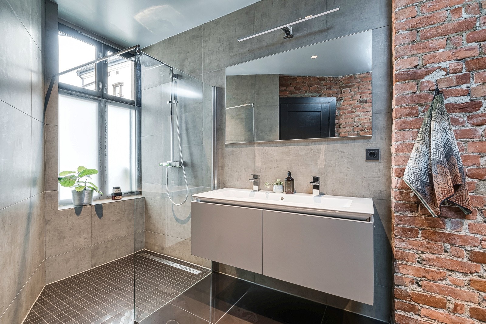 Badet er rent og delikat med grå innredning, dobbel servant og ulike fliser i fin kombinasjon. Galleribilde