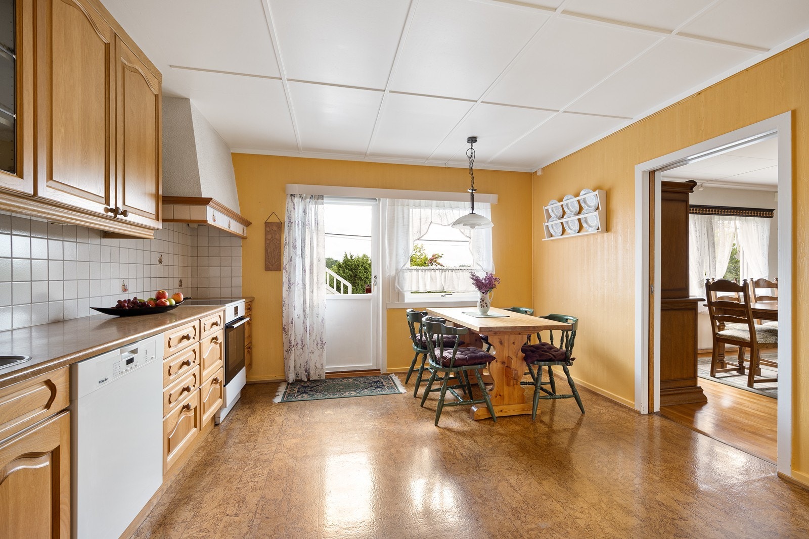 Innredningen har profilerte fronter, vitrineskap og laminatbenkeplate med dobbel oppvaskkum. Det er opplegg for oppvaskmaskin.
Fra kjøkkenet er det utgang til den ene terrassen. Galleribilde