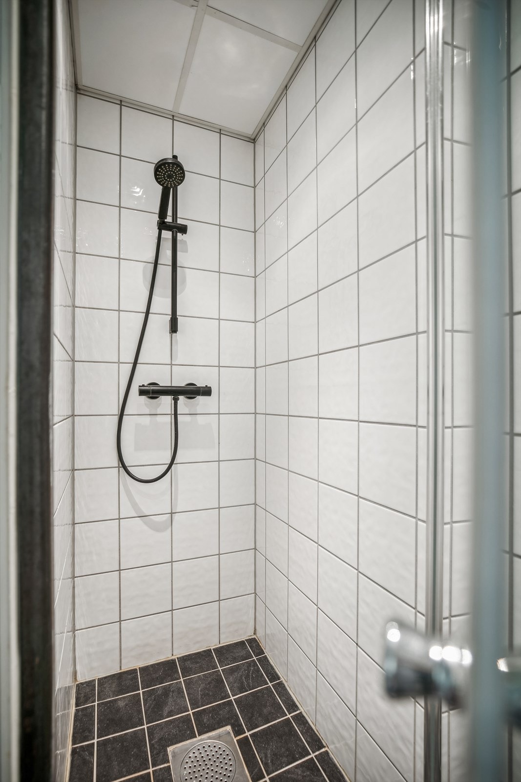 Badeeromsinnredningen består av veggmontert dusj direkte på gulv, veggmontert klosett, servant, speil og belysning. Galleribilde