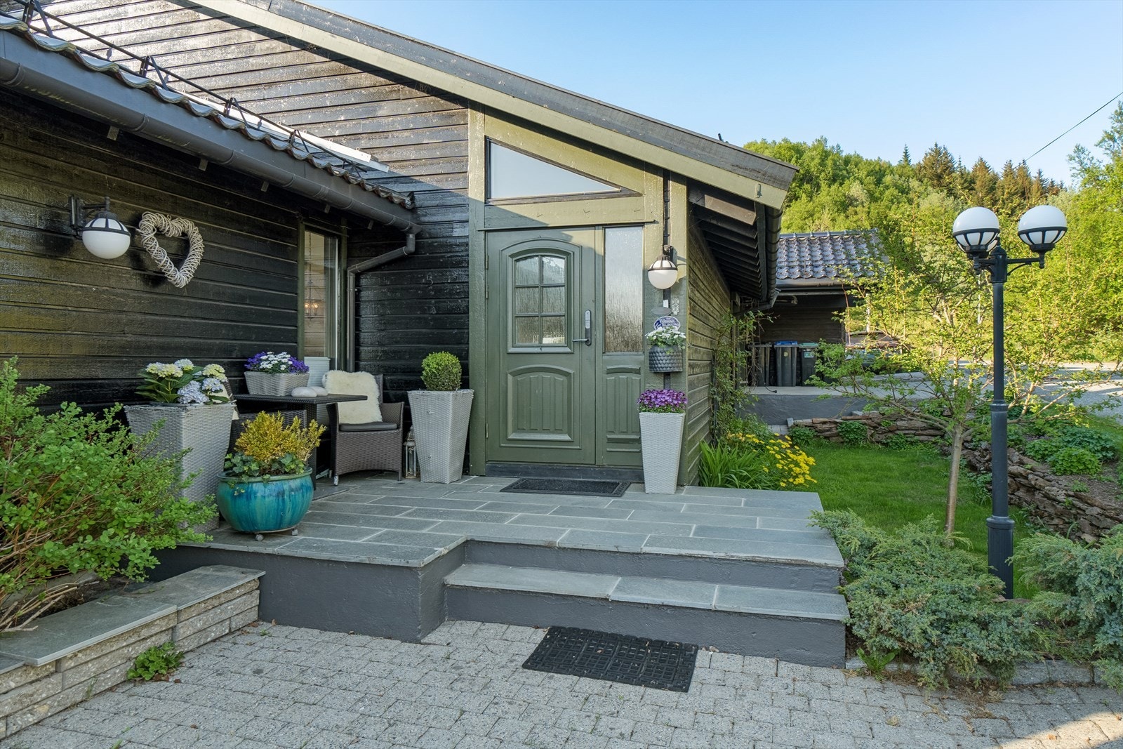 Inngangspartiet er innbydende med hellelagt uteplass, beplantning og belysning Galleribilde