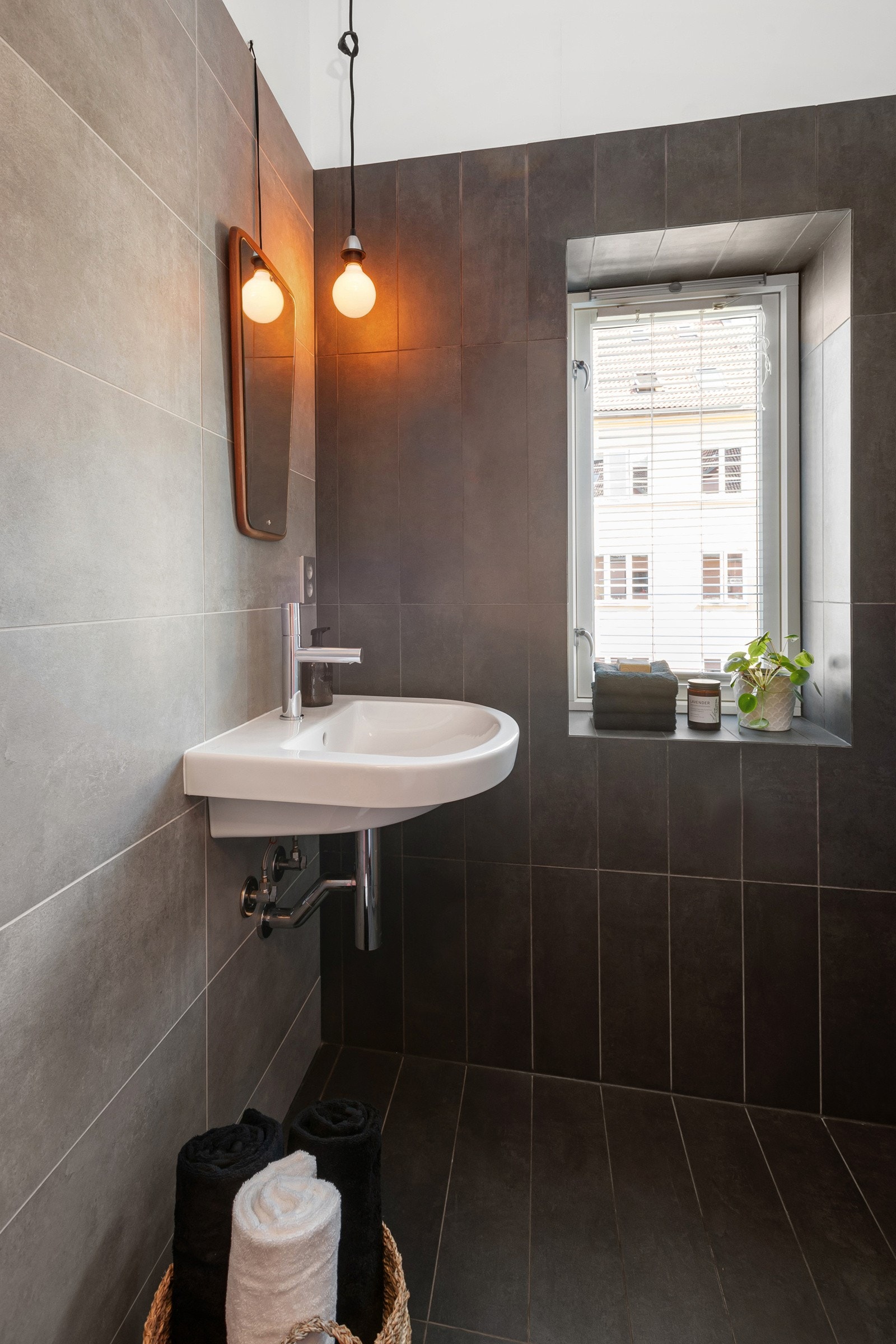 Badet har mørke og moderne fliser på vegger og gulv. Det er opplegg for vaskemaskin. Galleribilde