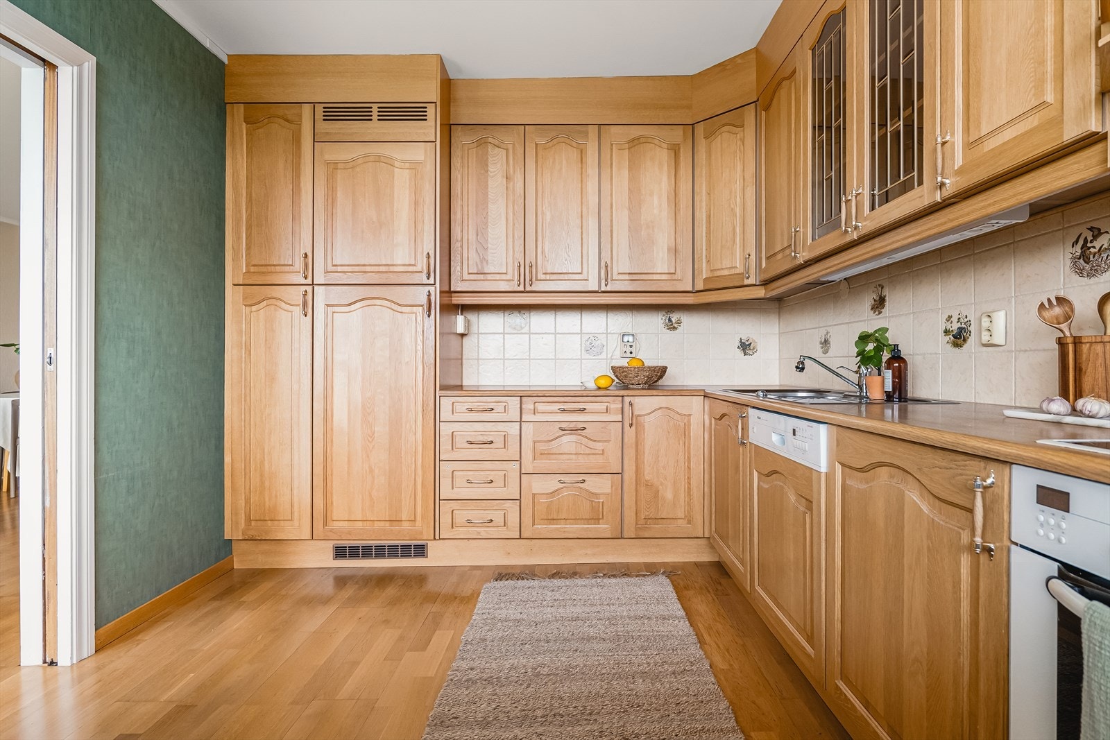 Laminat benkeplate, stål vaskekum og ventilator. Ventilatorrør på kjøkken går ut igjennom yttervegg. Keramiske fliser over benkeplate. Tre-stavs eikeparkett på gulv, tapet på vegger og malt betong i himling. Galleribilde