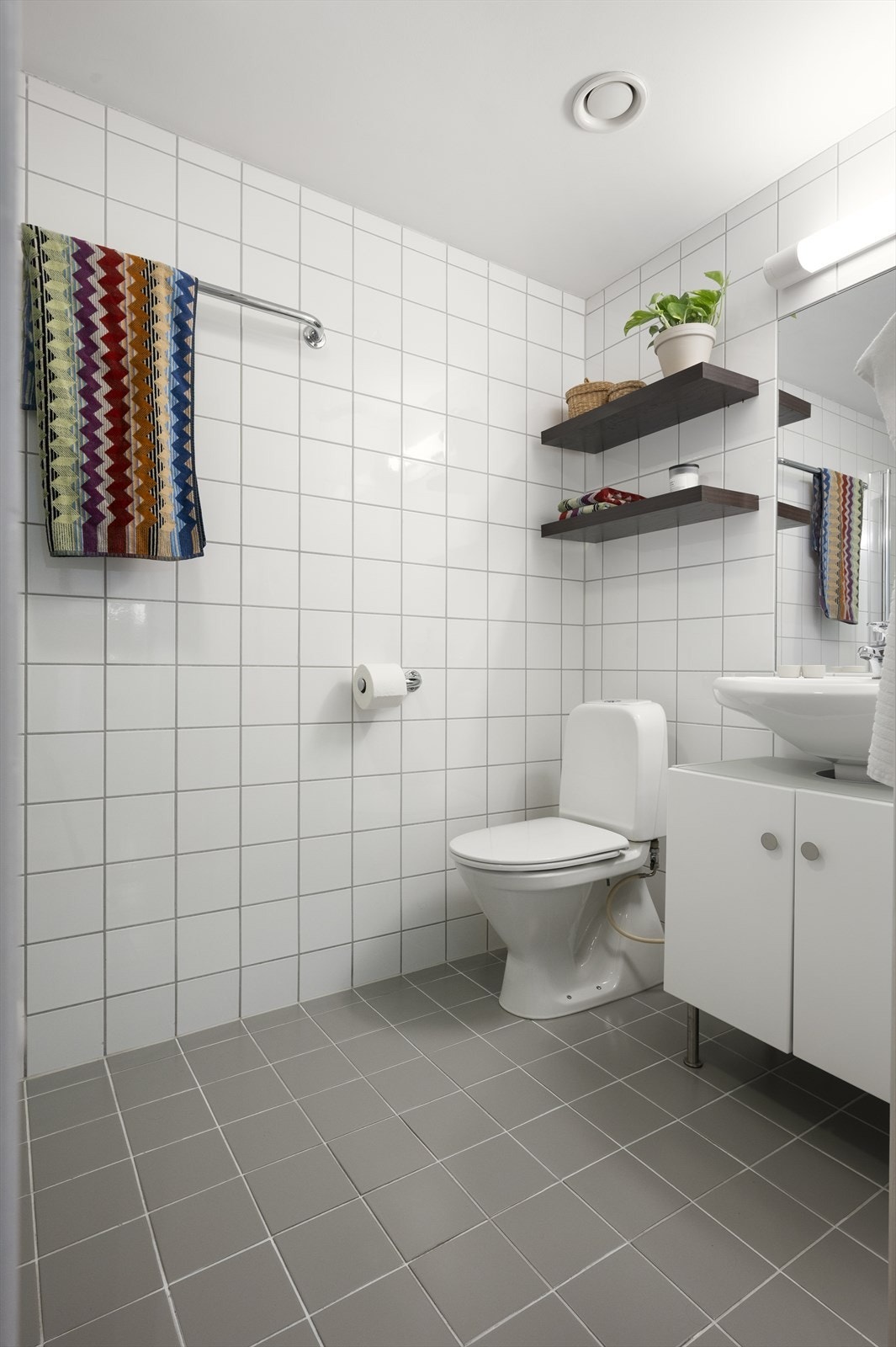Badet er innredet med vegghengt servantskap med servant og ett-greps armatur, speil med overlys og stikkontakt på vegg over servant. Det er installert hyller på veggen for ekstra oppbevaring. Galleribilde