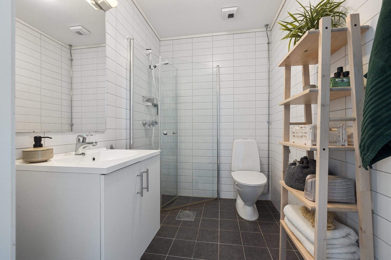 Pent, flislagt bad med dusjhjørne, servant med underskap og speil med lys. Galleribilde