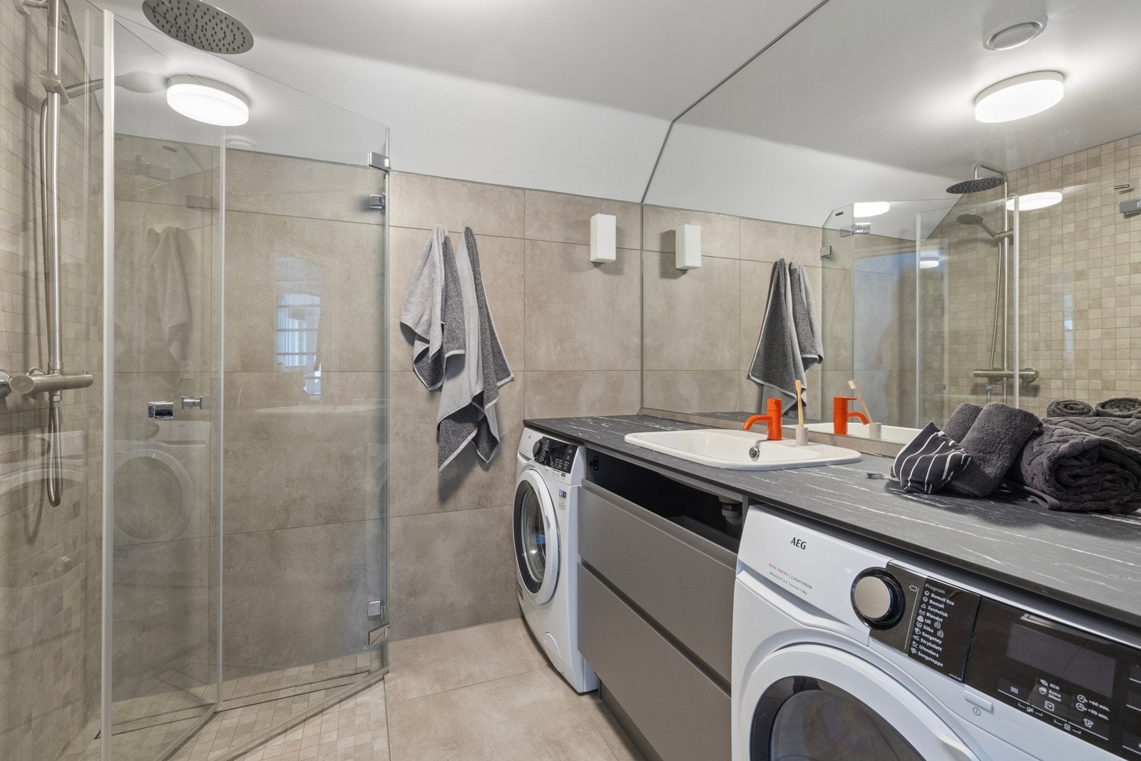 Flislagt baderom innredet med dusjnisje, servant med skuffeseksjon, klosett og benk med avsatt plass for vaskemaskin og tørketrommel. Galleribilde