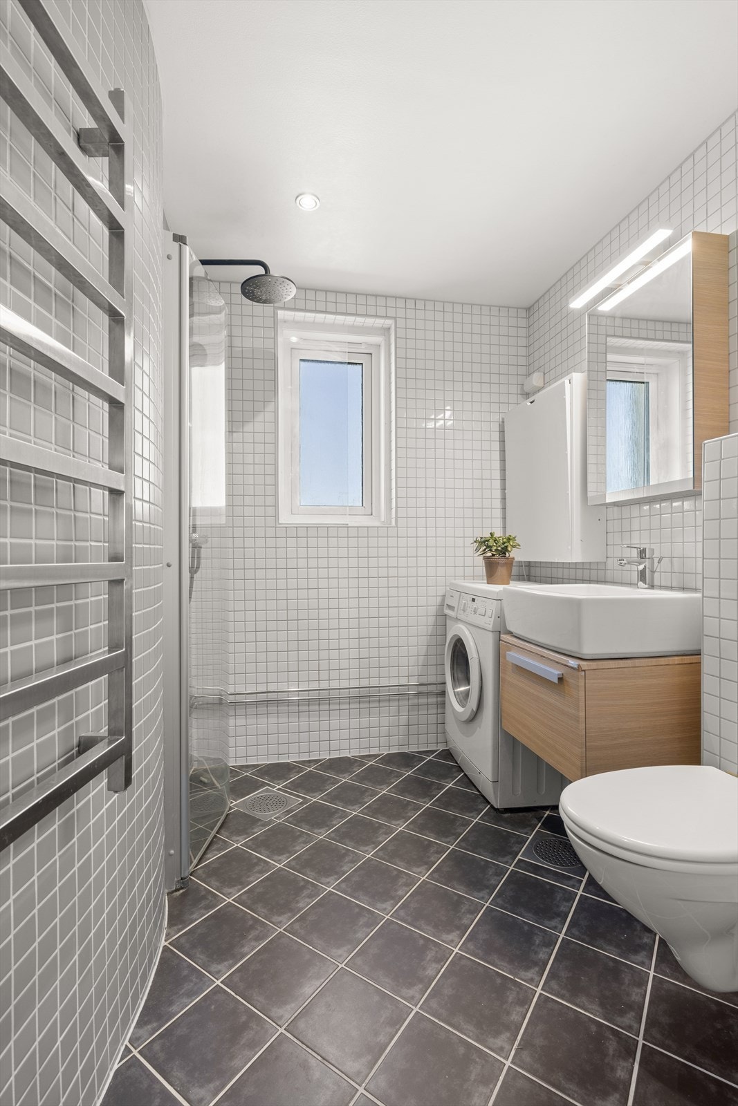 Badet er innredet med håndklevarmer, servantinnredning, dusjhjørne, klosett og vaskemaskin Galleribilde