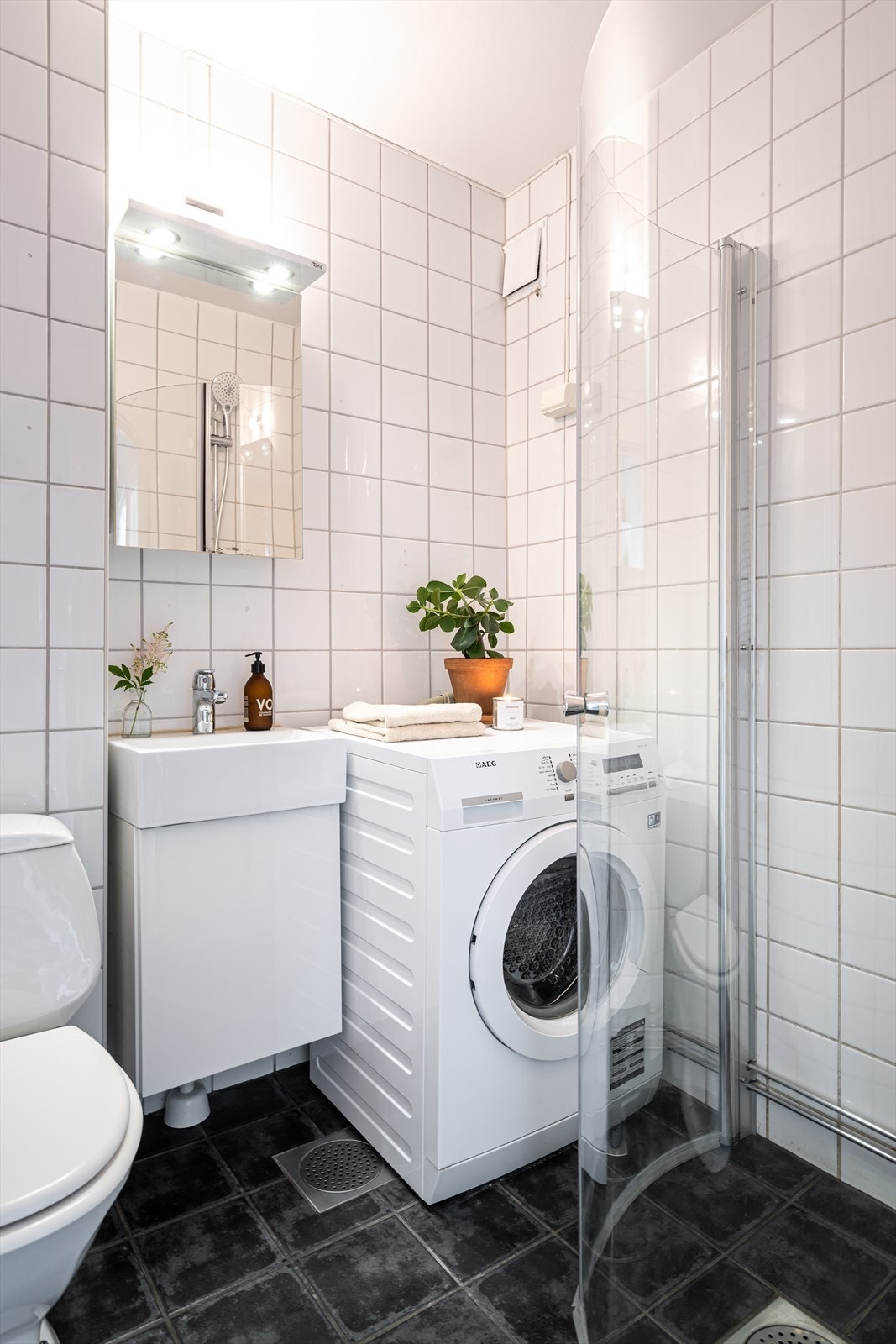 Badet har mørke fliser på gulv med gulvvarme, hvite fliser på veggene og opplegg for vaskemaskin. Galleribilde