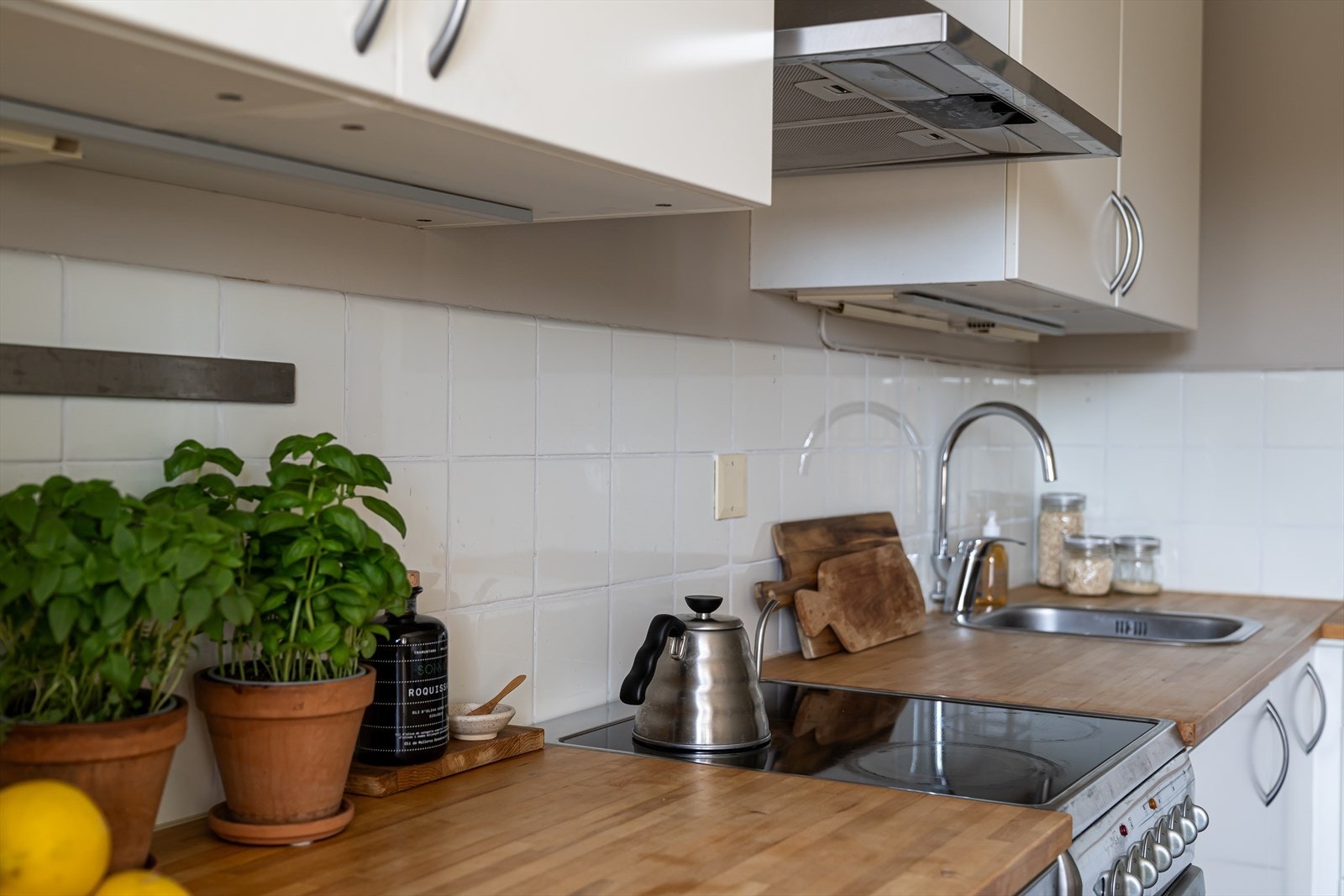 Innredningen er plassert i L-form, med takoppforede skap, hvite, glatte fronter, benkeplate i heltre med nedfelt vaskekum, og hvite fliser over benken. Galleribilde