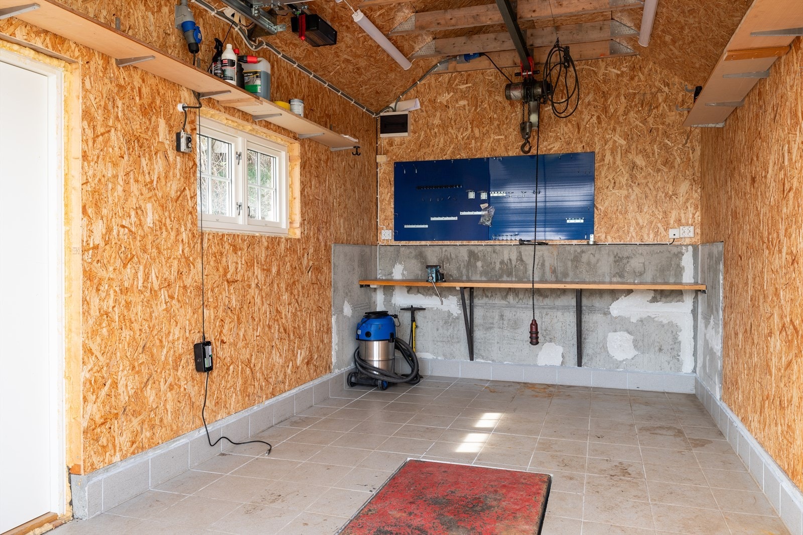 Garasjen er isolert, med løftbukk i gulv, vinsj og kompressor montert i hanebjelkene. Det er etablert el-billader. Galleribilde