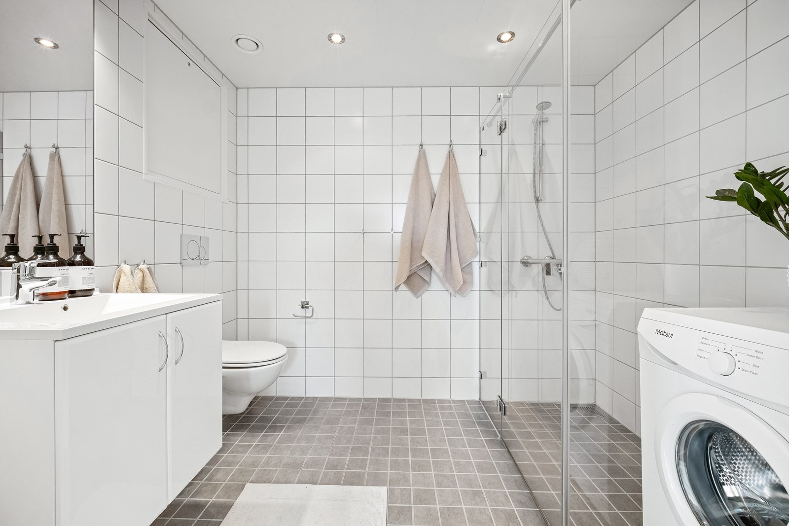 Pent bad med vegghengt toalett, servant med skap og romslig dusjsone med glassvegg og glassdør. Galleribilde