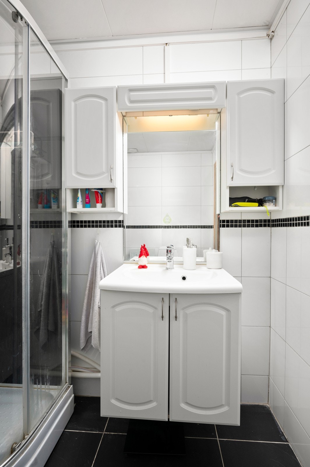 Badet er utstyrt med servant i innredning med underskap og overskap med speil i mellom Galleribilde