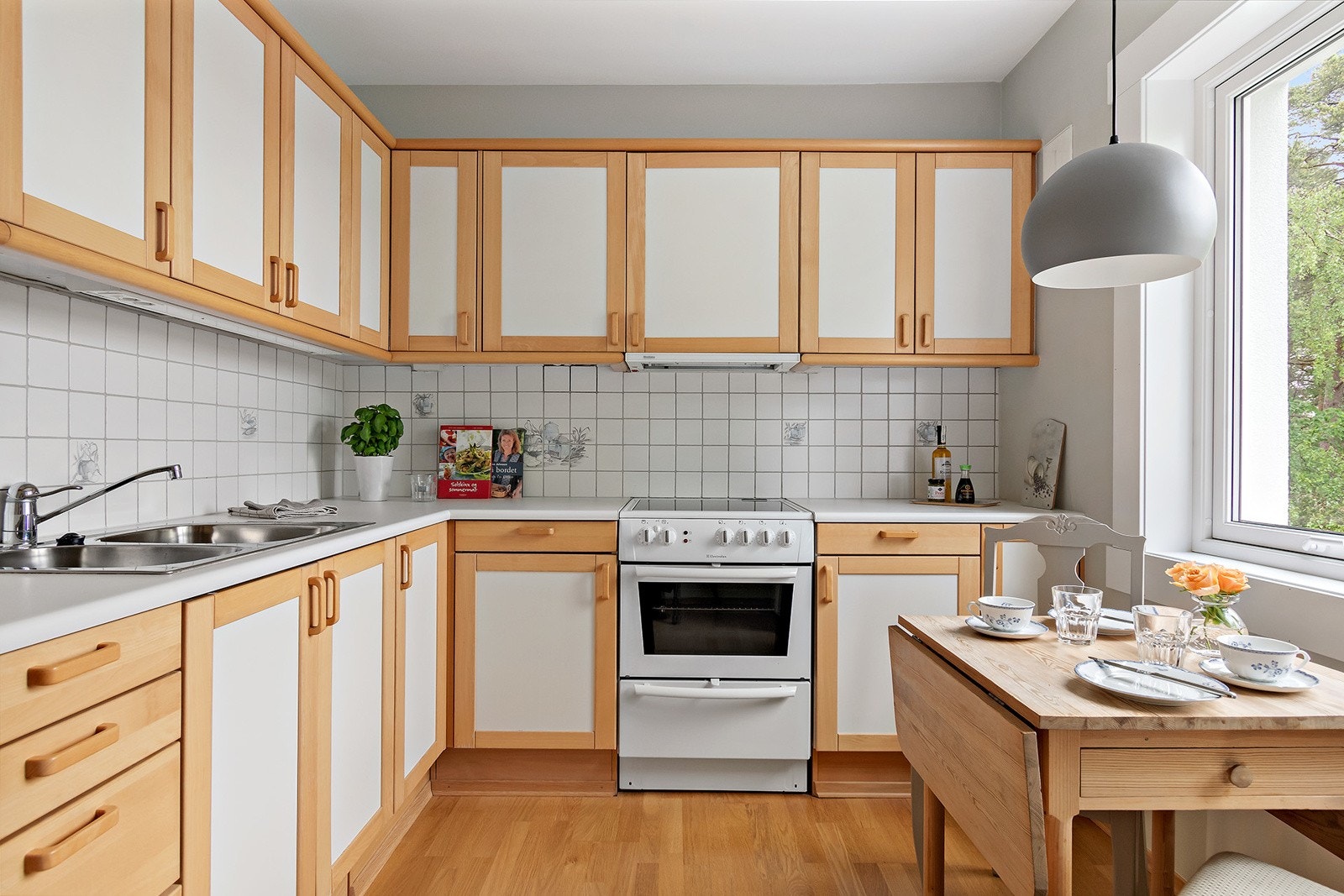 Kjøkkeninnredning med glatte finerte skapfronter, laminat benkeplate med fliser på bakvegg, dobbel oppvaskkum, ventilator og frittstående hvitevarer som komfyr, kjøl/- fryseskap. Galleribilde