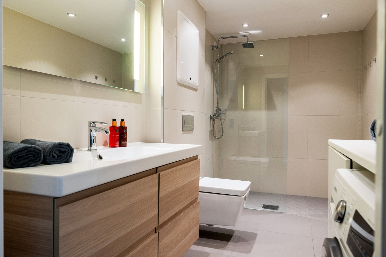 Badet er innredet med dusjhjørne med regnfalls- og håndholdt garnityr og veggmontert klosett med innebygget sisterne. Galleribilde