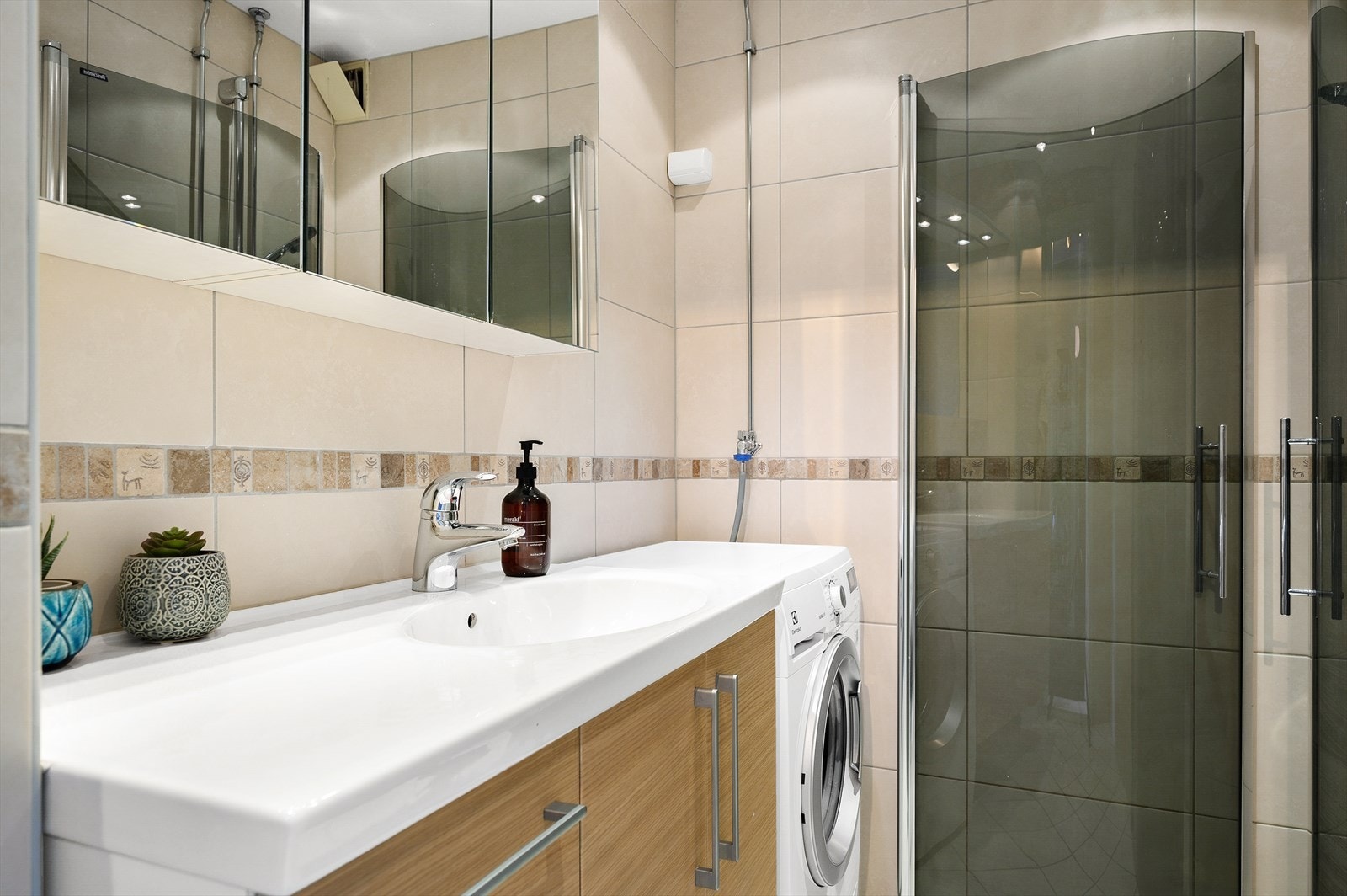 Innredningen bestående av servant med innredning, speil og skap over servant. Dusjhjørne med innfellbare dører i herdet glass. Galleribilde