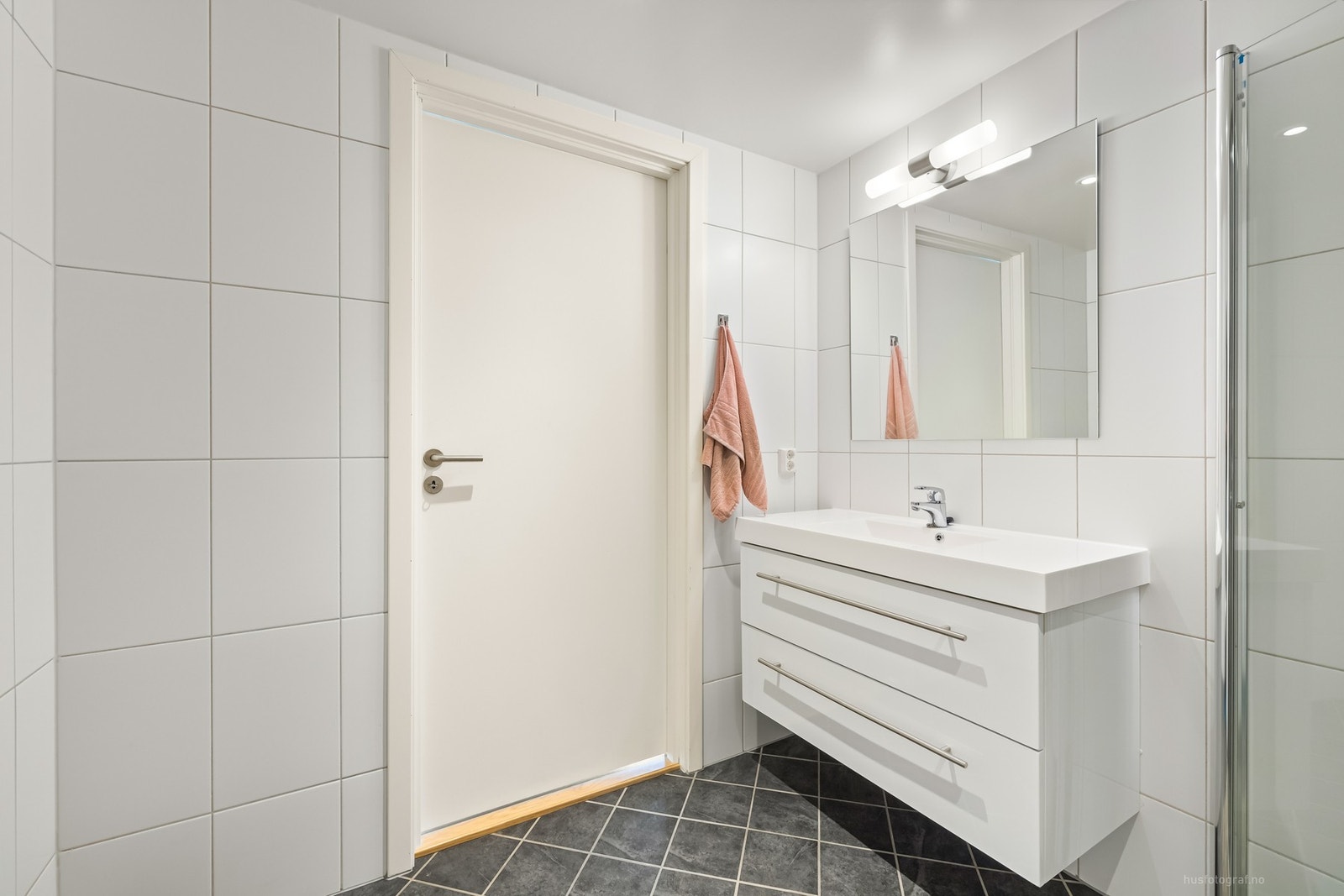 Badet har vegghengt toalett, servant på innredning og dusjhjørne med foldedører i glass, for optimal utnyttelse av gulvarealet. Galleribilde