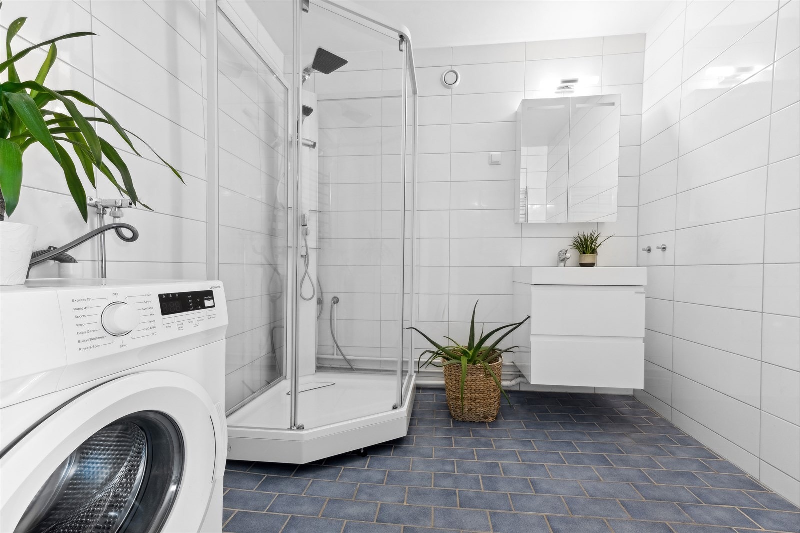 Badet er flislagt og har en enkel, moderne innredning med slette fronter. Servanten er heldekkende, og den har et praktisk ettgreps blandebatteri og avløpsrør av plast. Galleribilde