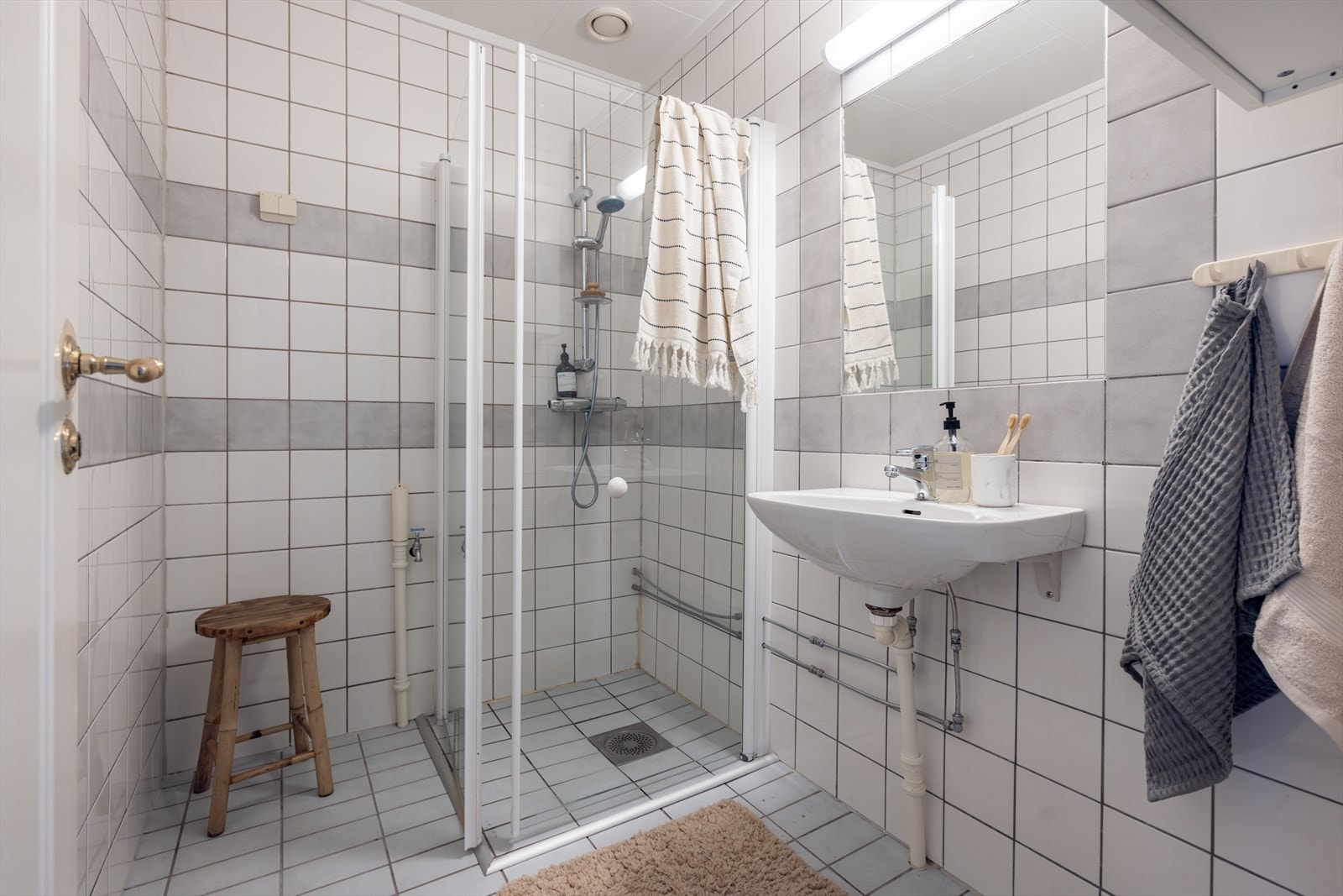 Eldre flislagt bad, innredet med dusj og servant. Badet har behov for oppgradering. Galleribilde