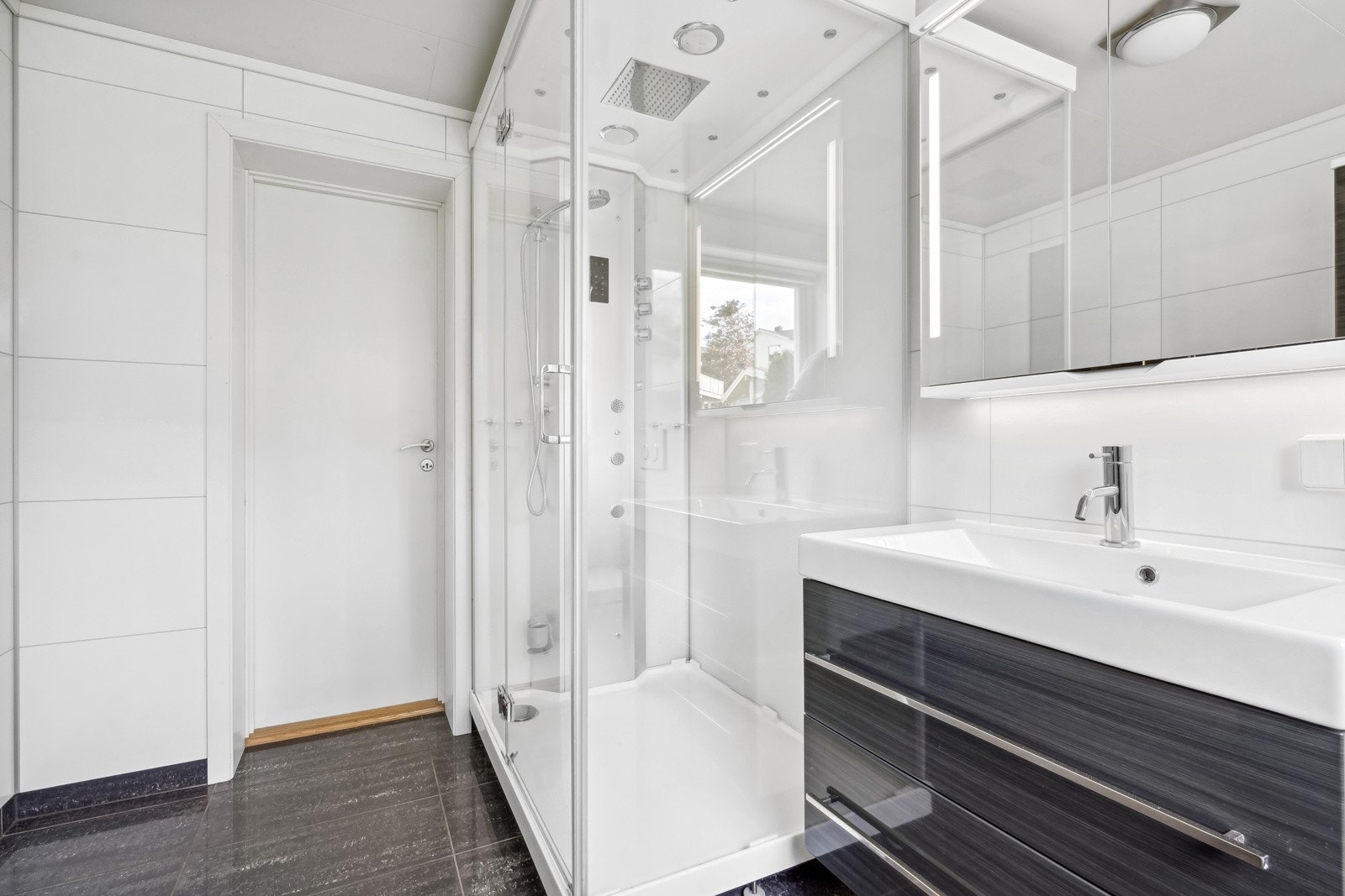 Flott flislagt bad i utleiedel utstyrt med et romslig dusjkabinett og vegghengt servantskap. Galleribilde