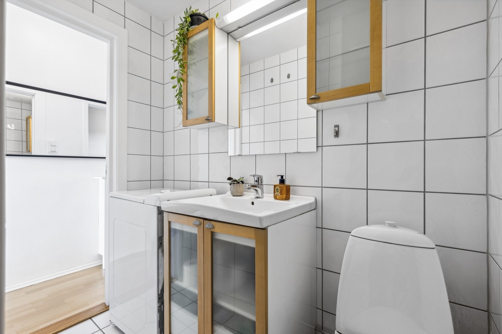 Badet er innredet med servant og underskap, et speil med belysning over, samt to vegghengte skap på hver side. I tillegg finnes et gulvmontert klosett. Med gulvvarme og plass til en liten vaskemaskin er dette et komfortabelt og funksjonelt rom. Galleribilde
