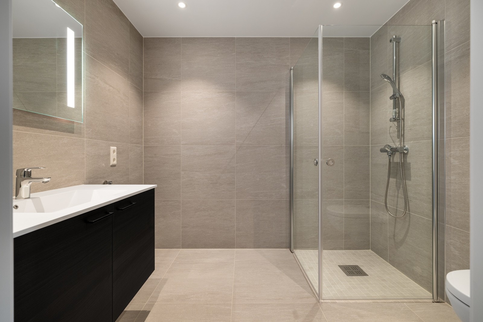 Lekkert og moderne baderom med flislagte gulv- og veggflater. Behagelig varme i gulv. Pen baderomsinnredning og speil med belysning. Downlights i himling. Galleribilde