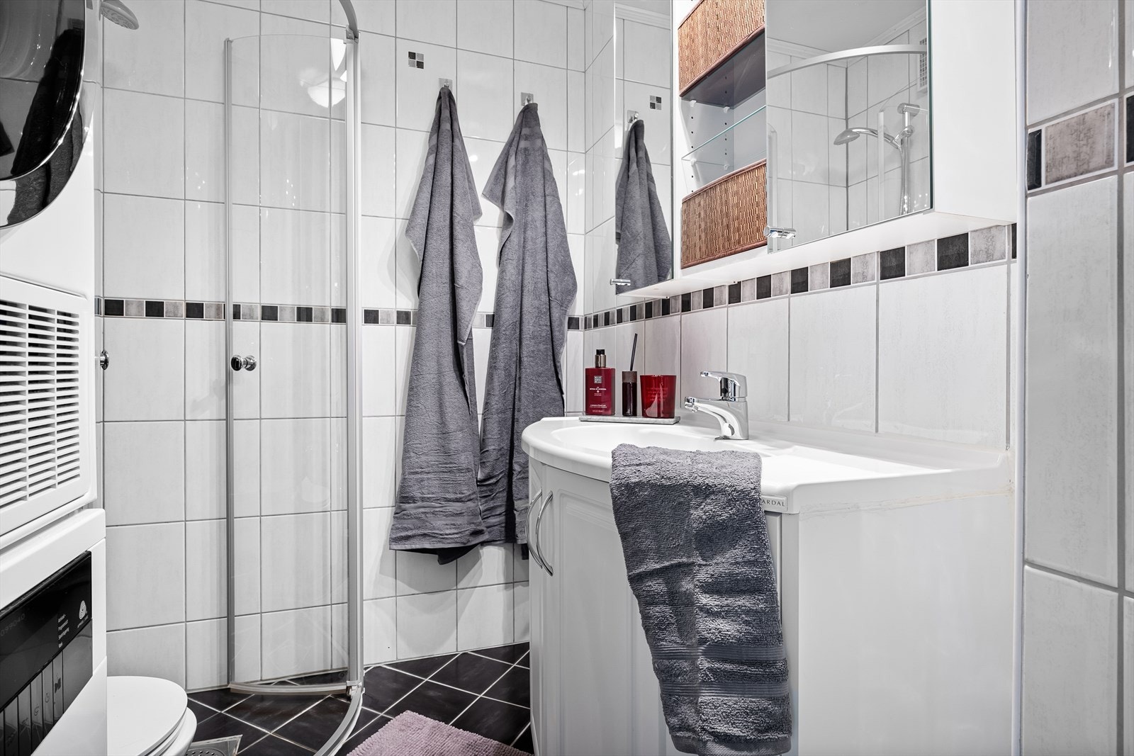 Flislagt bad med dusjhjørne, veggfestet wc, vask med skap og opplegg for vaskemaskin Galleribilde