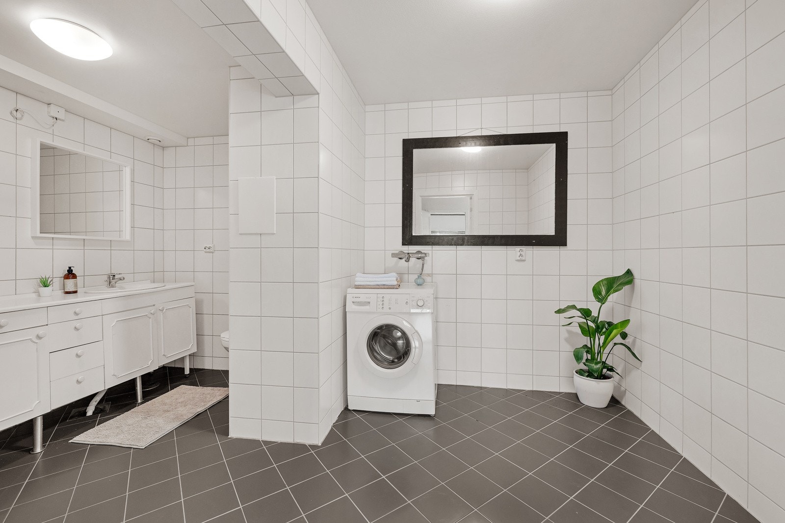 Badet er av god størrelse og er kledd i lyse fliser på vegger, med mørke fliser på gulv Galleribilde
