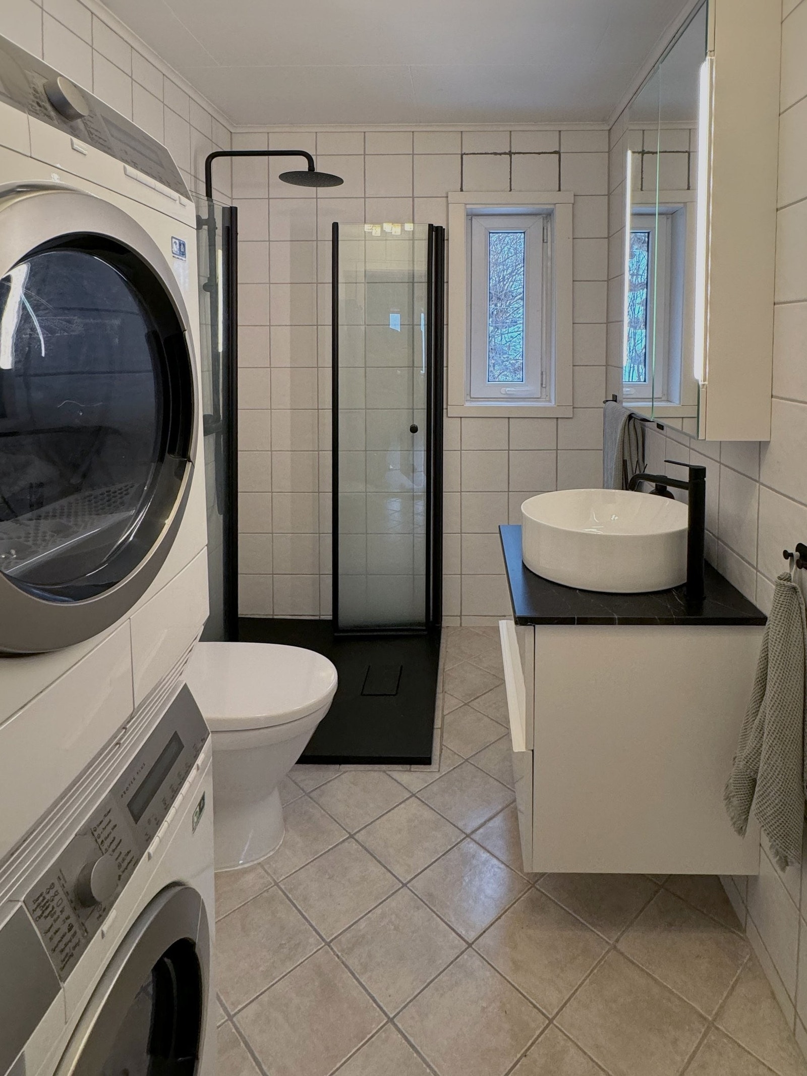 Modernisert bad fra 2023. Lyst og flislagt baderom med servantskap med skuffer, speilskap med belysning, dusjvegger, toalett og opplegg for vaskemaskin. Galleribilde