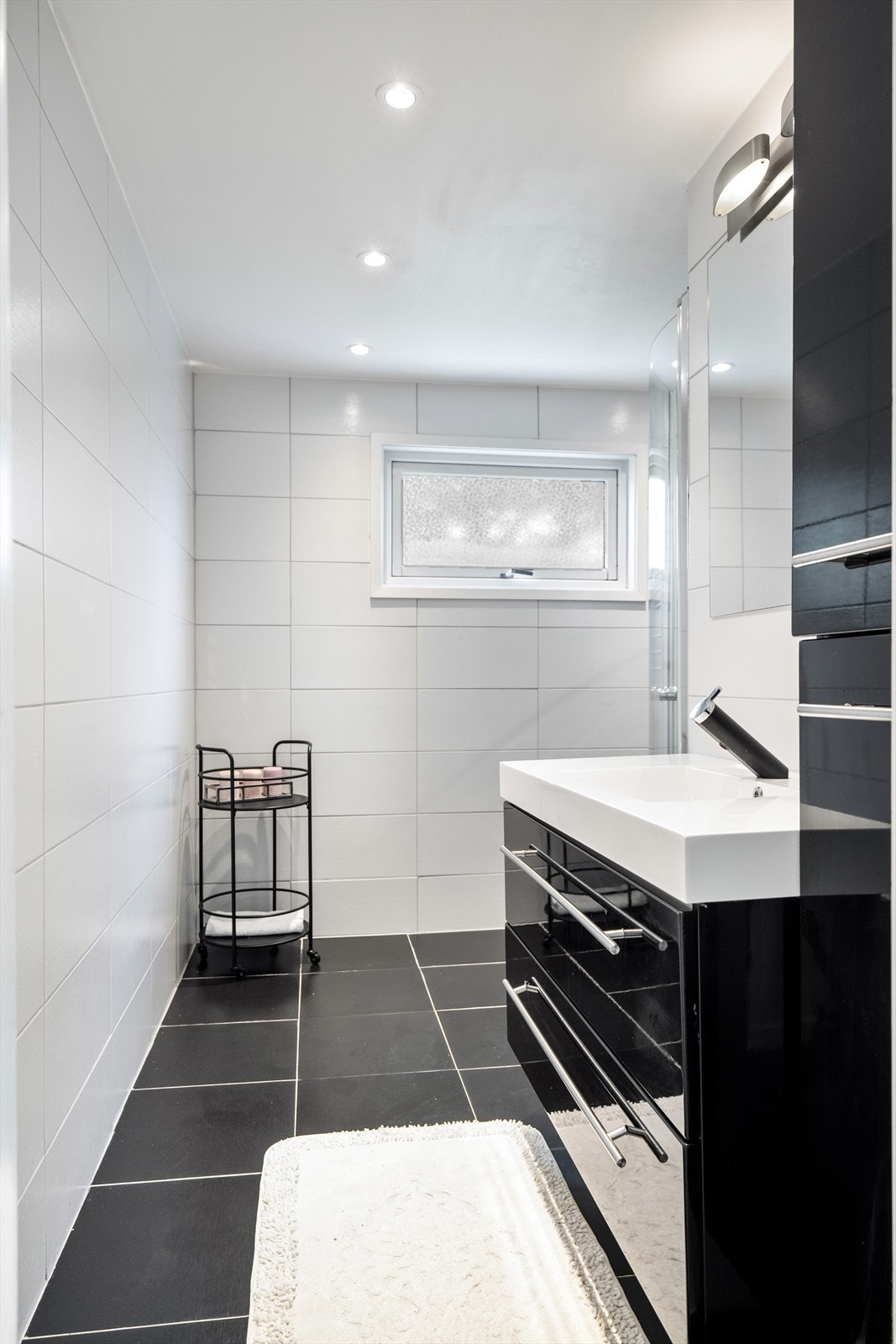 Baderommet er flislagt og inneholder servant med underskap- og sideskap, dusjhjørne med innfellbare dusjdører og håndklevarmer. Galleribilde