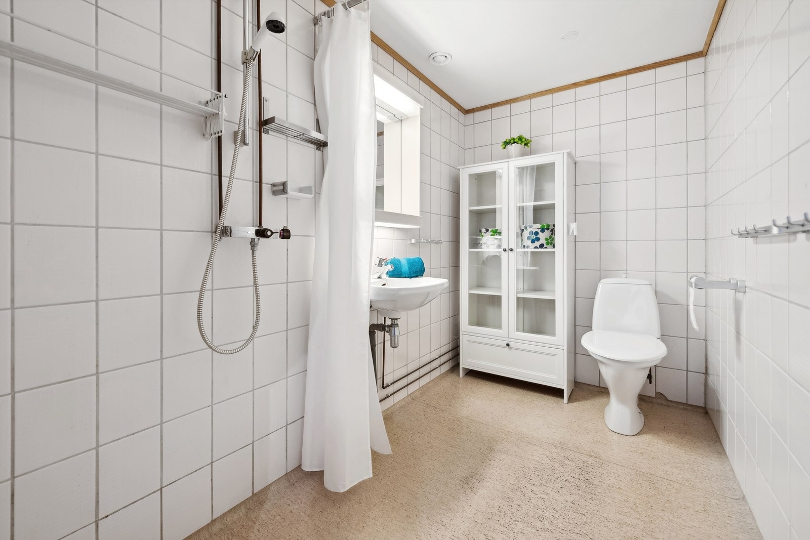 Innredning består av en enkel servant, gulvstående toalett, speil, og dusjnisje med forheng. Galleribilde