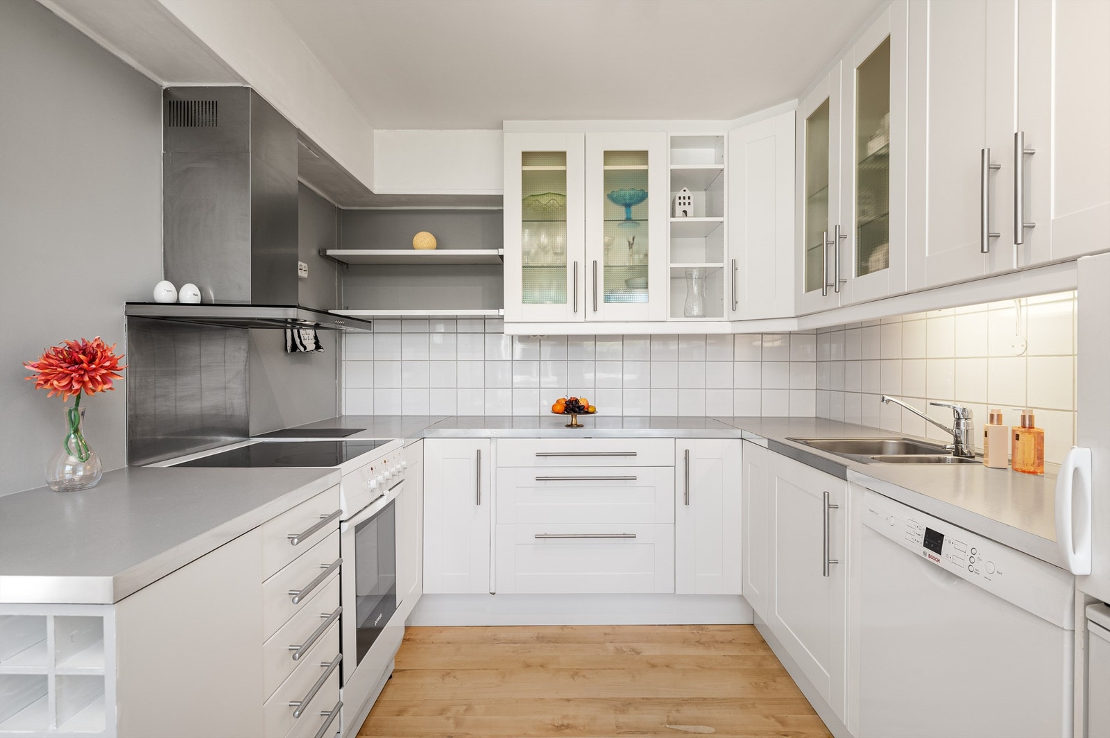 Pen kjøkkeninnredning fra IKEA med frittstående komfyr, oppvaskmaskin, kjøleskap og fryser. Det er lagt fliser mellom kjøkkenbenken og overskapene. Galleribilde