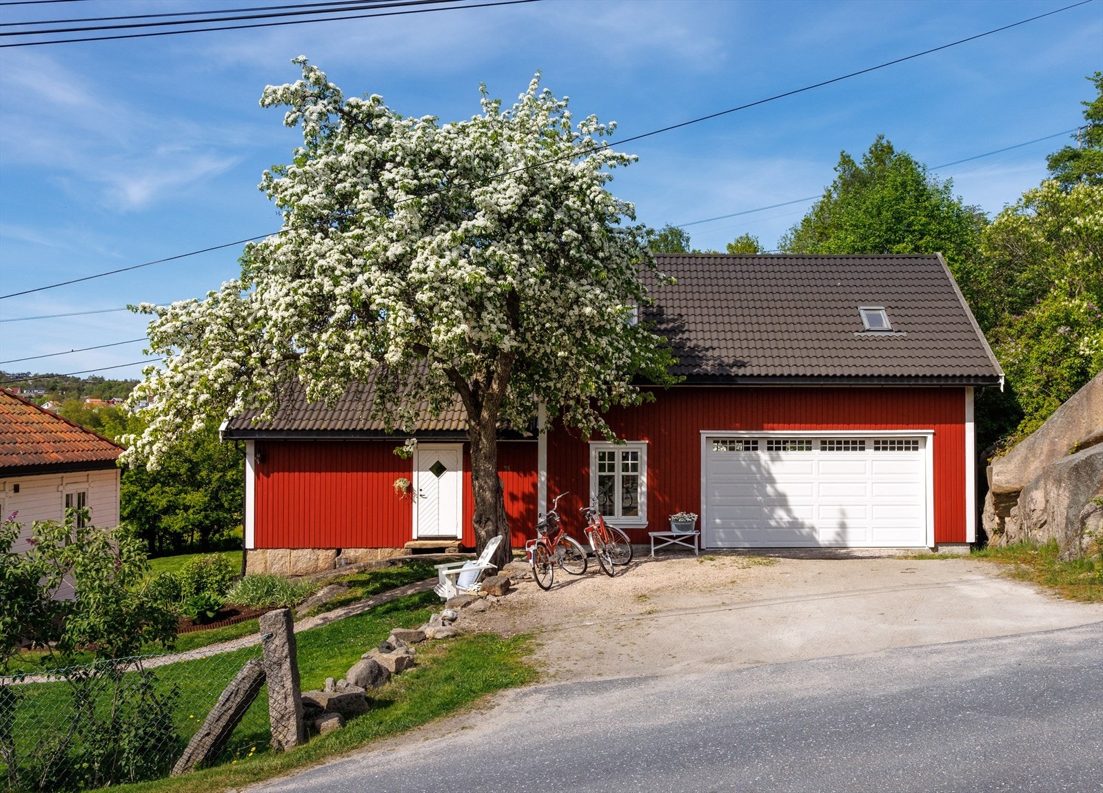 Ved innkjørselen står en garasje som likner en låve. Den er nesten like stor som boligen selv, er rødmalt med hvite karmer og strekker seg over to etasjer. Galleribilde