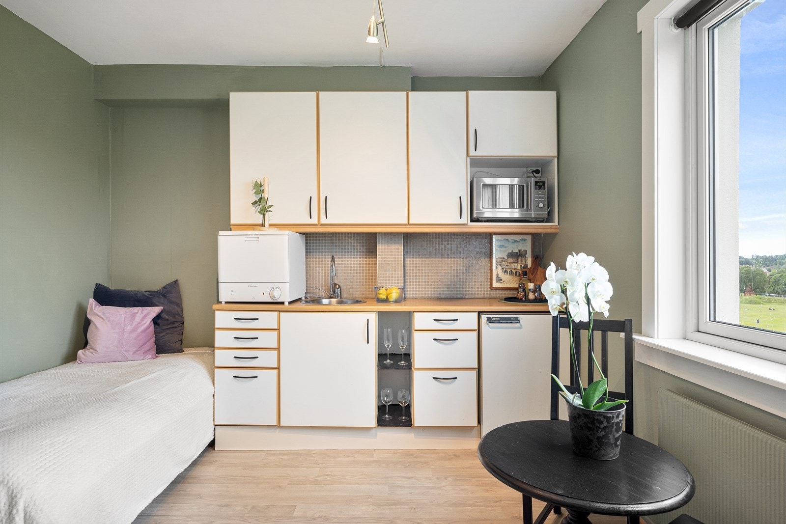 Lys kjøkkeninnredning bestående av hvit laminert kjøkkeninnredning med bjørkelister og glatte dørfronter, fliser mellom overskap og laminert benkeplate, kum med ettgreps blandebatteri og
lys/lyslist under overskap. Opplegg til vaskemaskin. Galleribilde