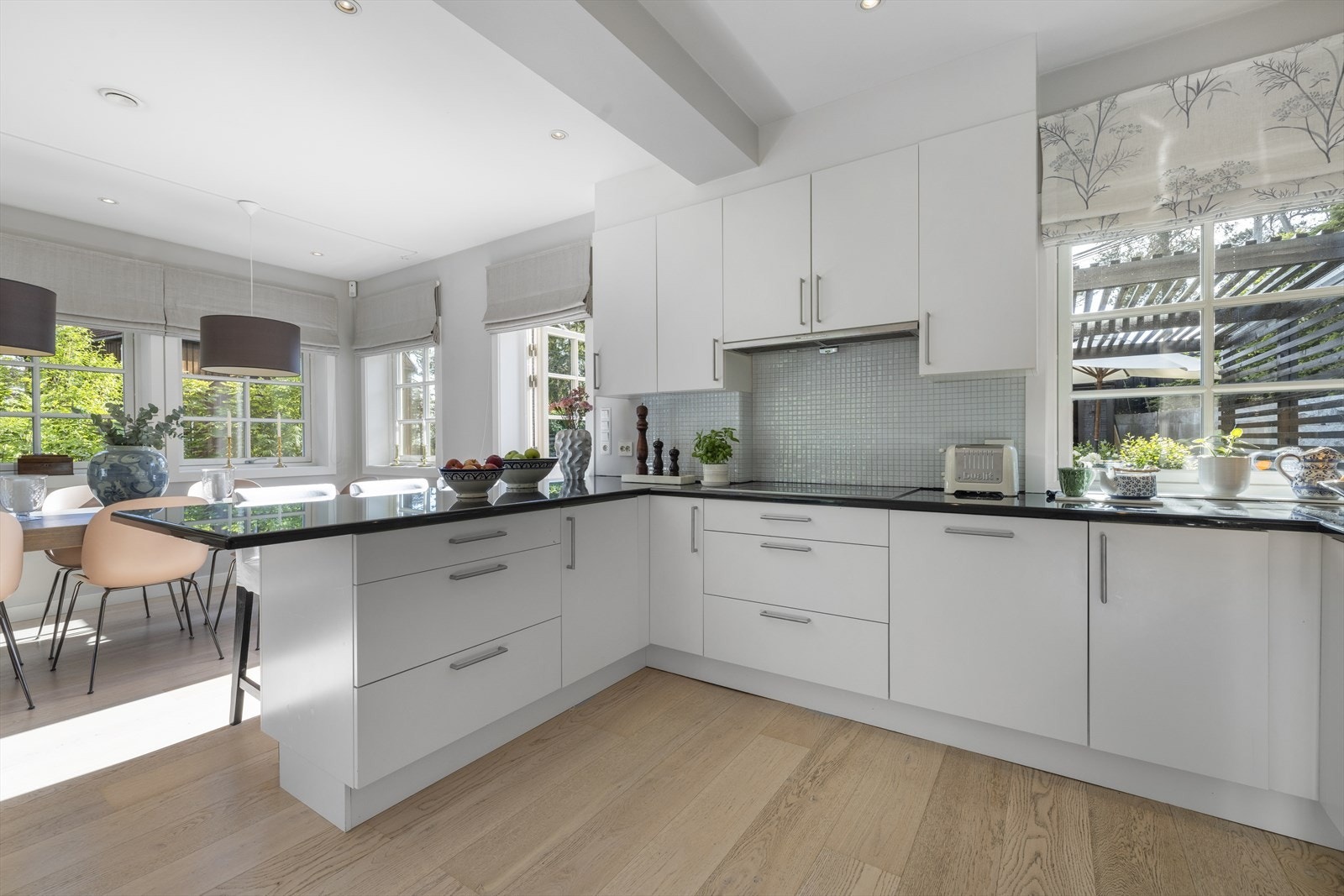 Innredning med hvite glatte fronter på skuffer og skap. Mosaikkfliser på vegg mellom benk og overskap Galleribilde