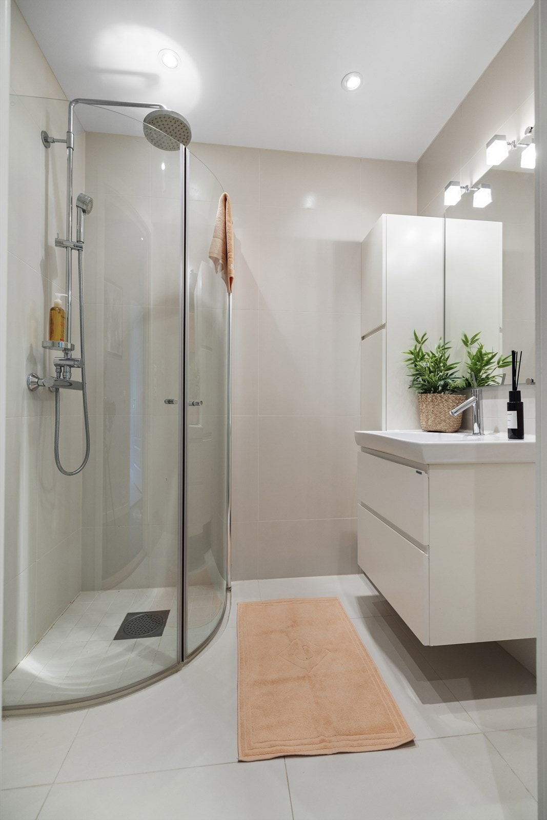 Dusjbad med støpt og flislagt gulv. Flislagte vegger og malt himling med innfelte downlights. Badet har innredning med nedfelt servant og dusjvegger/-hjørne Galleribilde